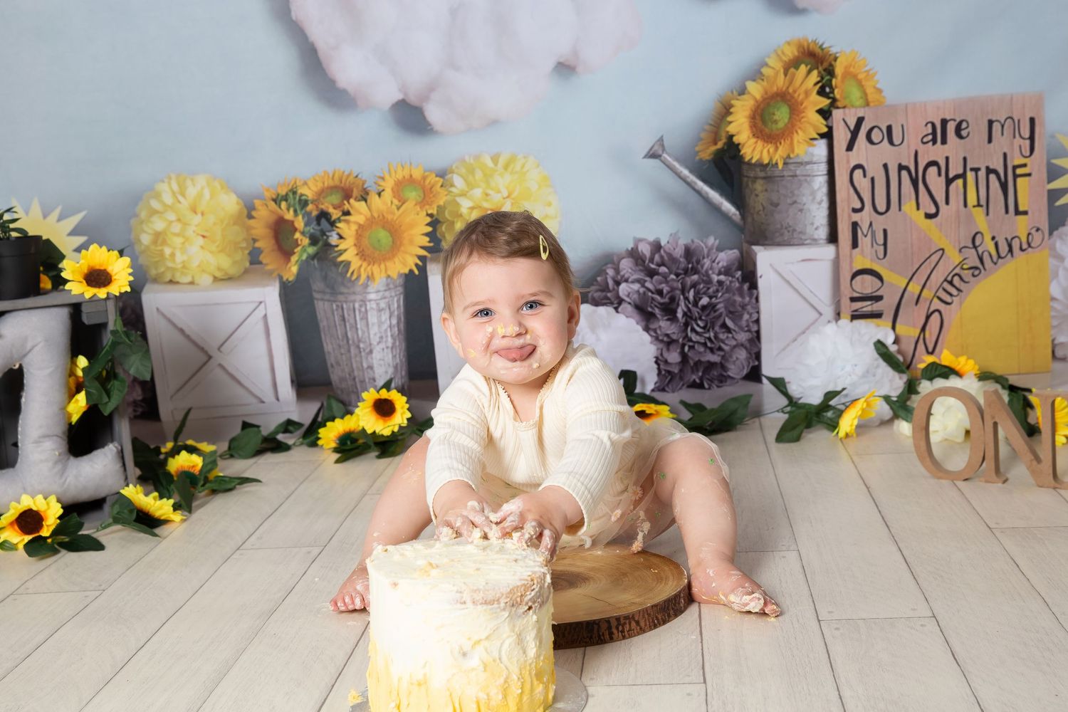 A first birthday cake smash photo session with yellow sunflower decorations and rustic wooden elements.