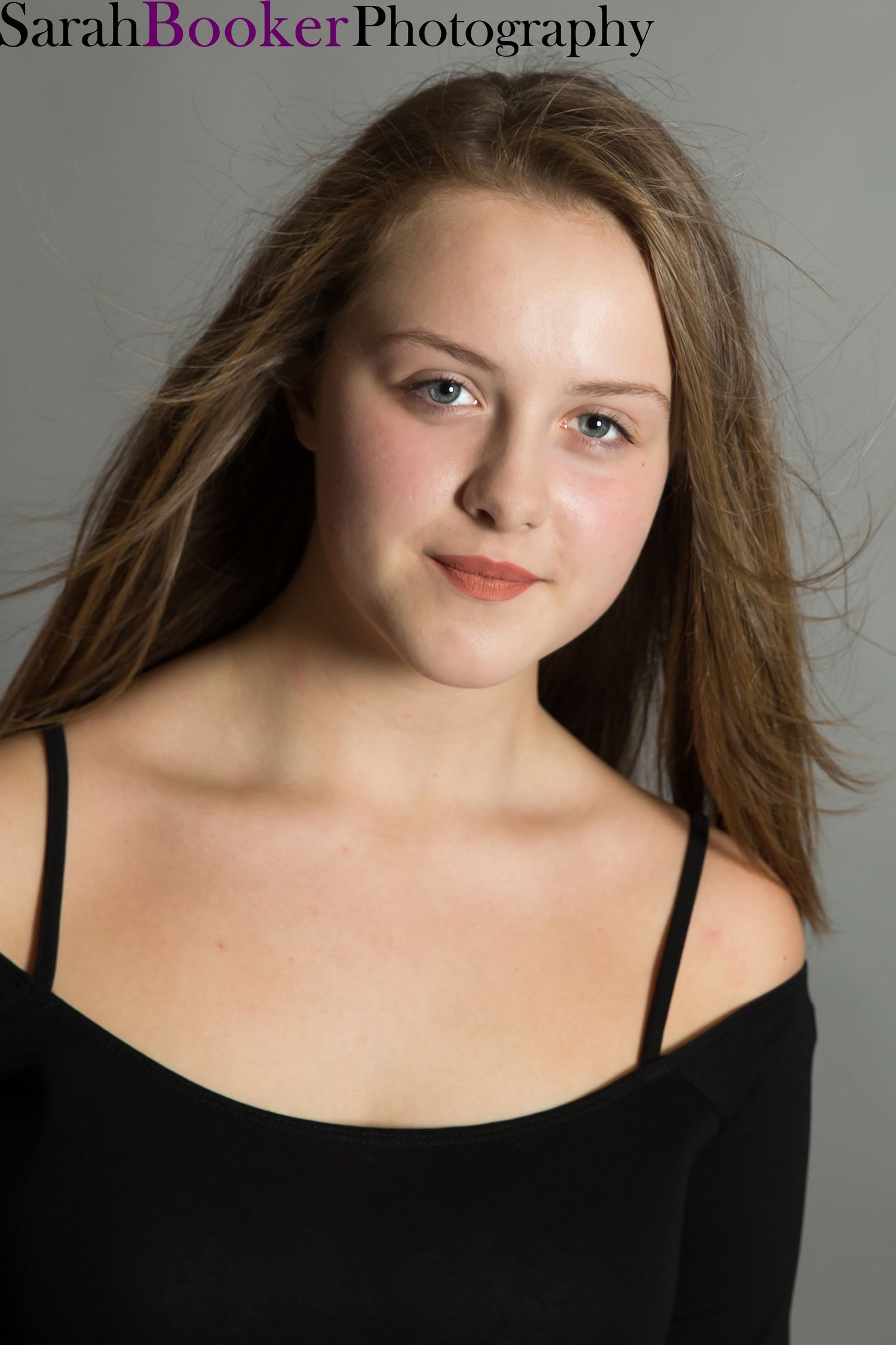 Professional portrait in soft lighting showing a young woman in a black top against neutral background.
