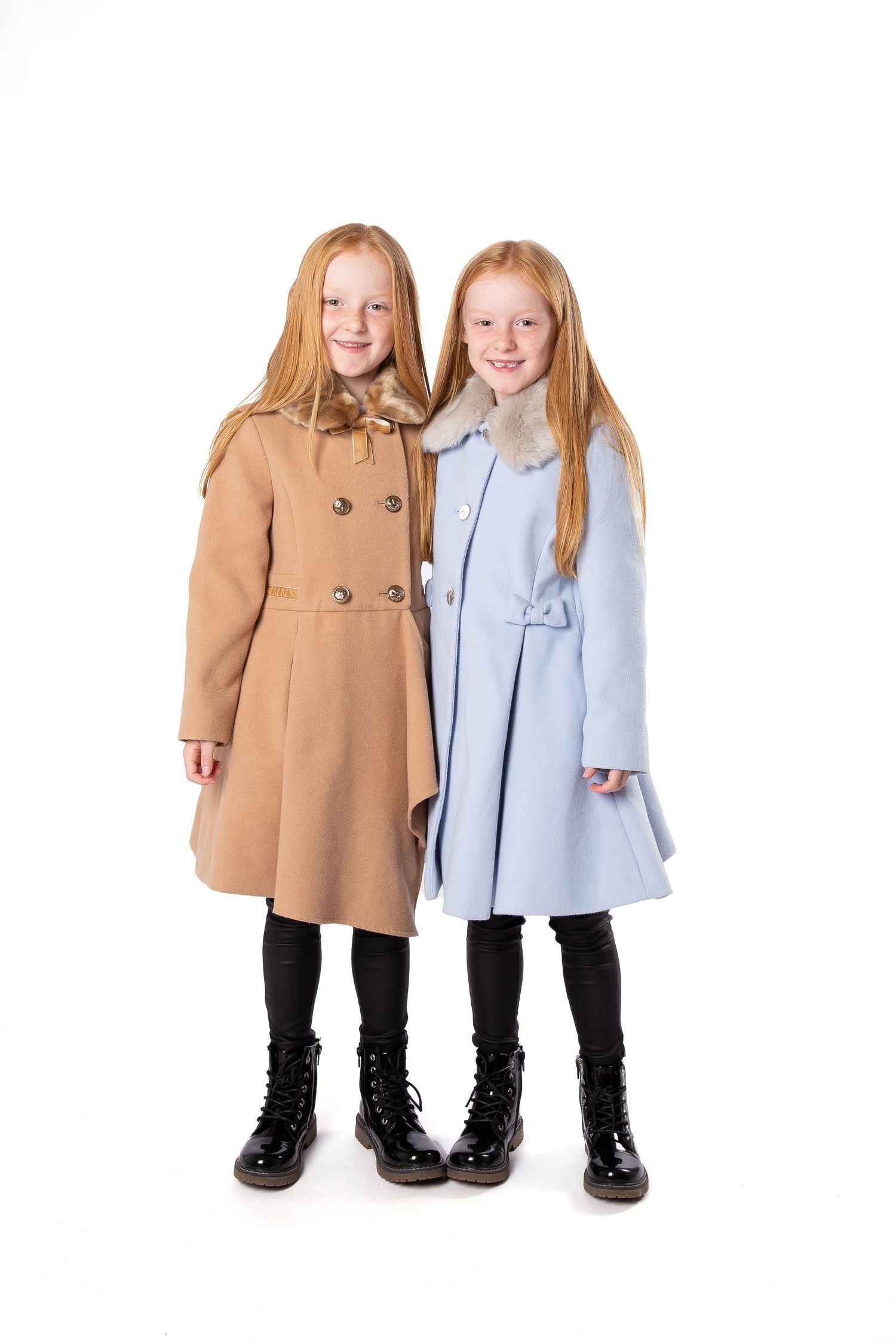Two figures standing together wearing winter dress coats in tan and light blue with black boots on white background.