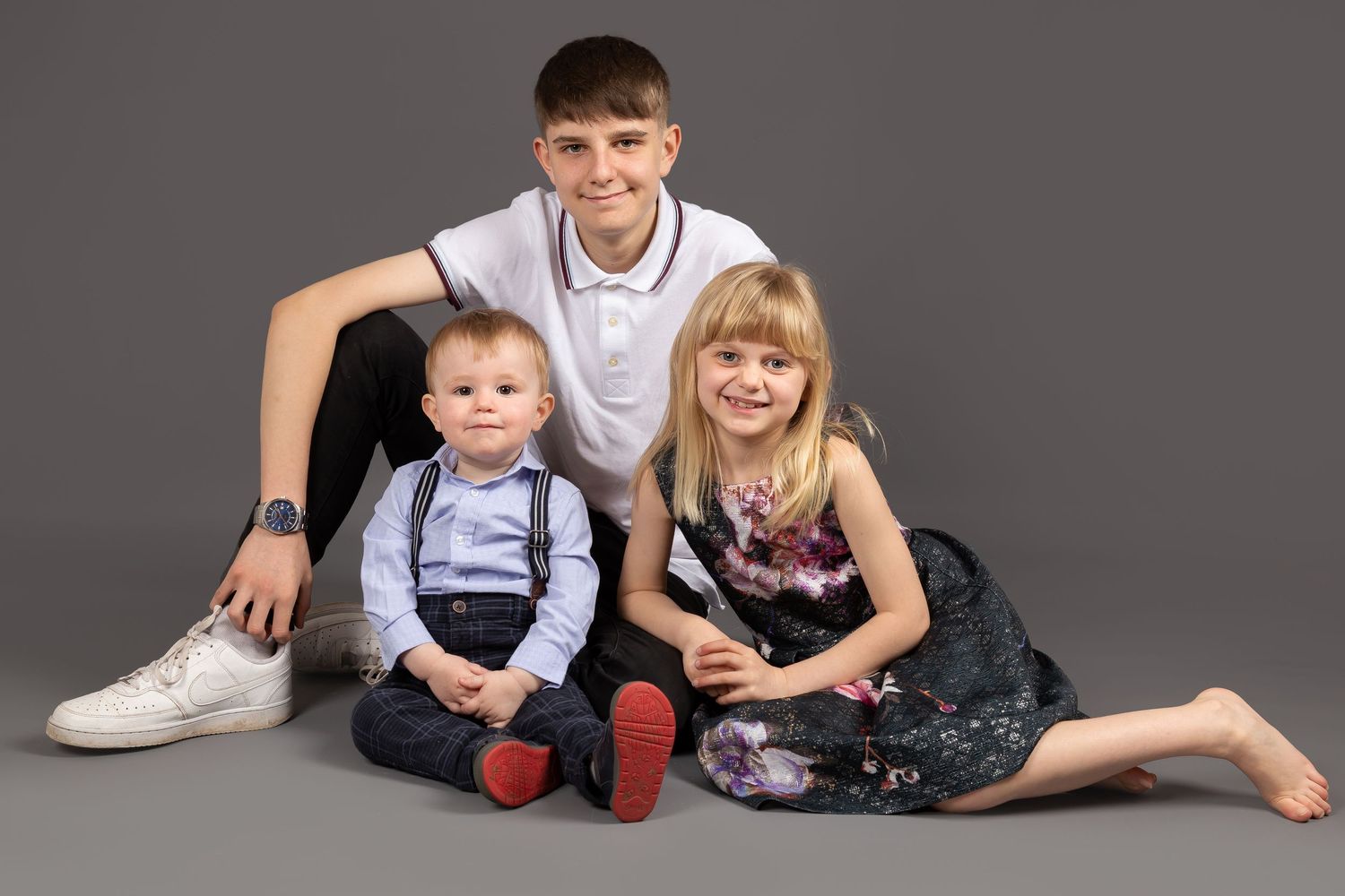 Three children posing together for a portrait against a gray backdrop.