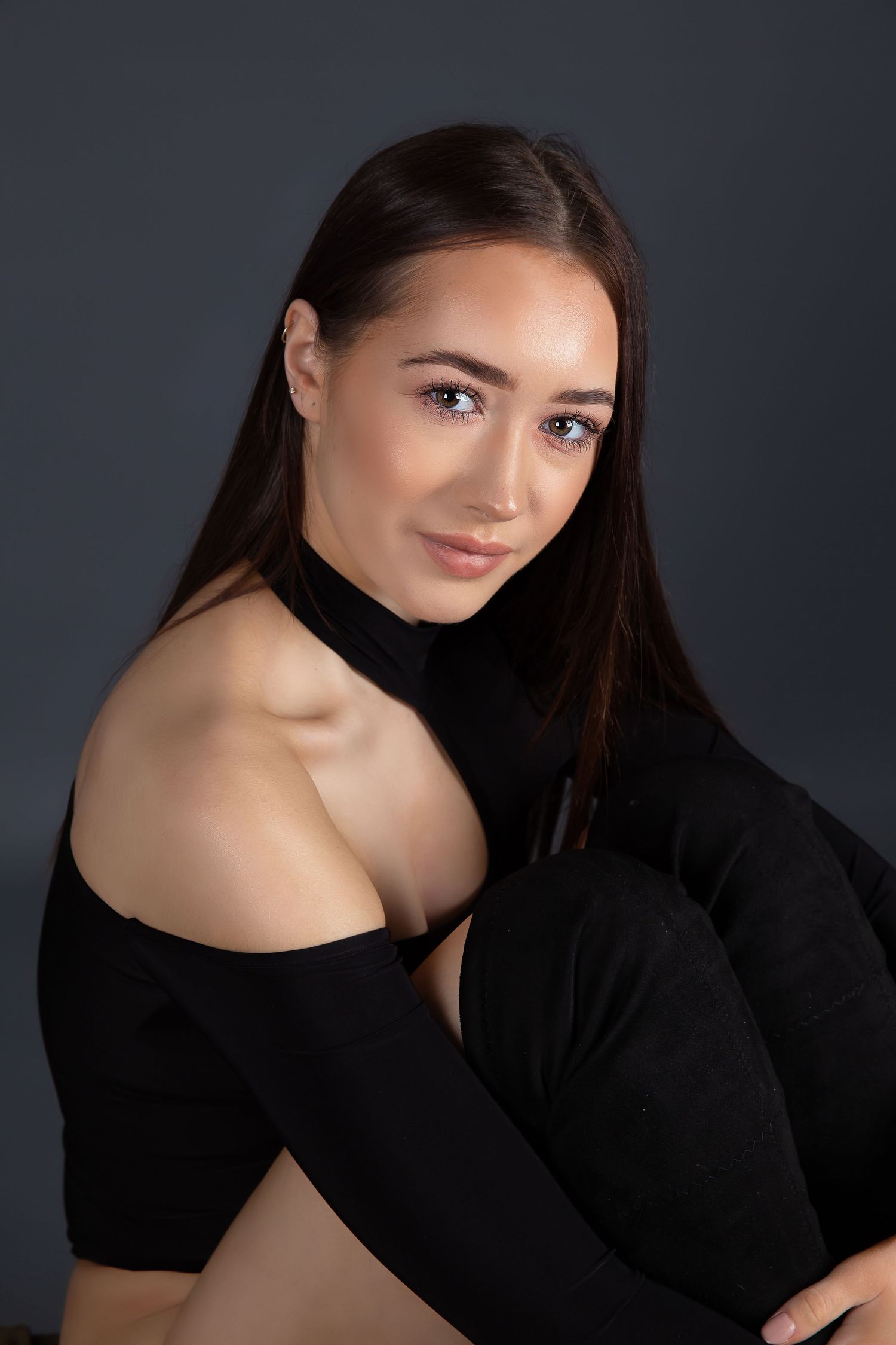 Studio portrait of someone in a black off-shoulder top against dark background.