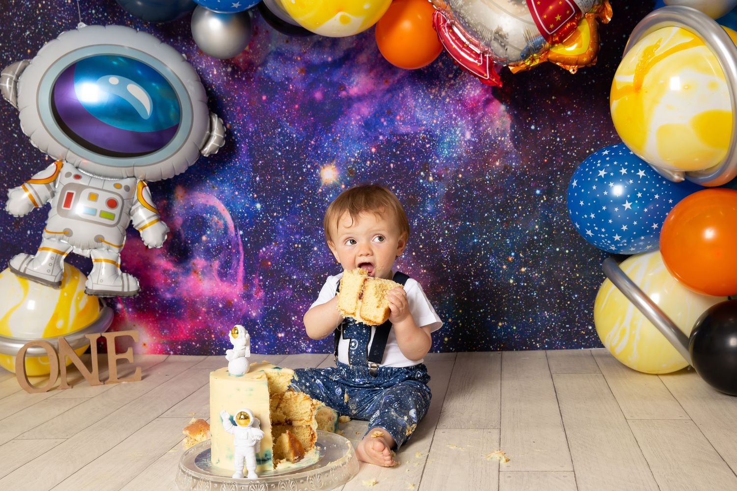 A space-themed party setup with colorful balloons, galaxy backdrop, and astronaut decorations against a starry background.