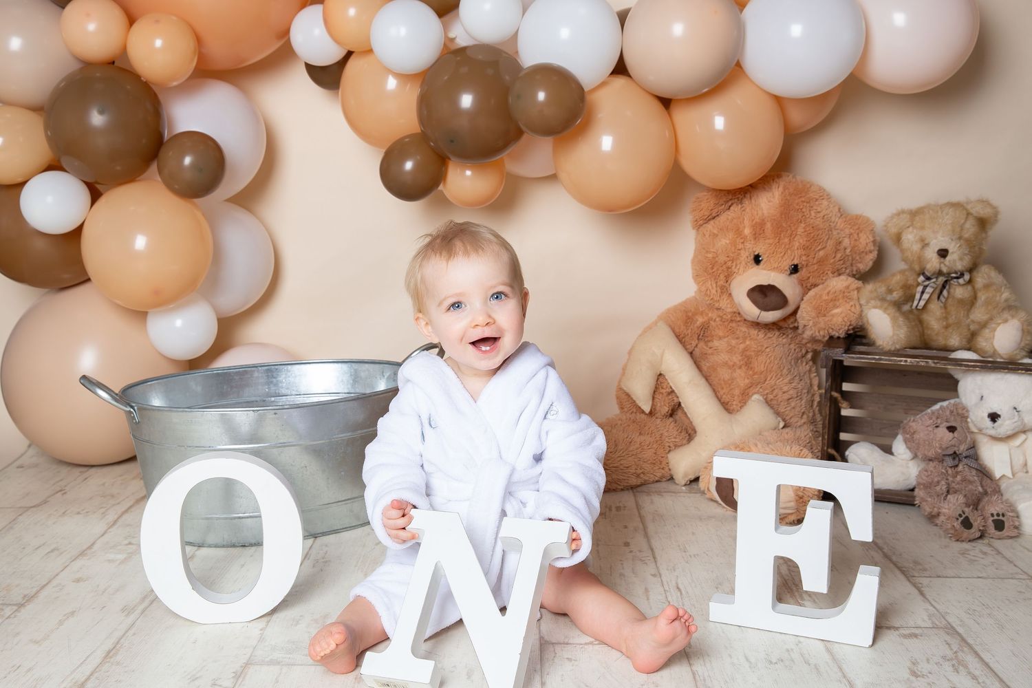 Balloon arch with beige and white colors serves as backdrop for decorative letter display against neutral wall.