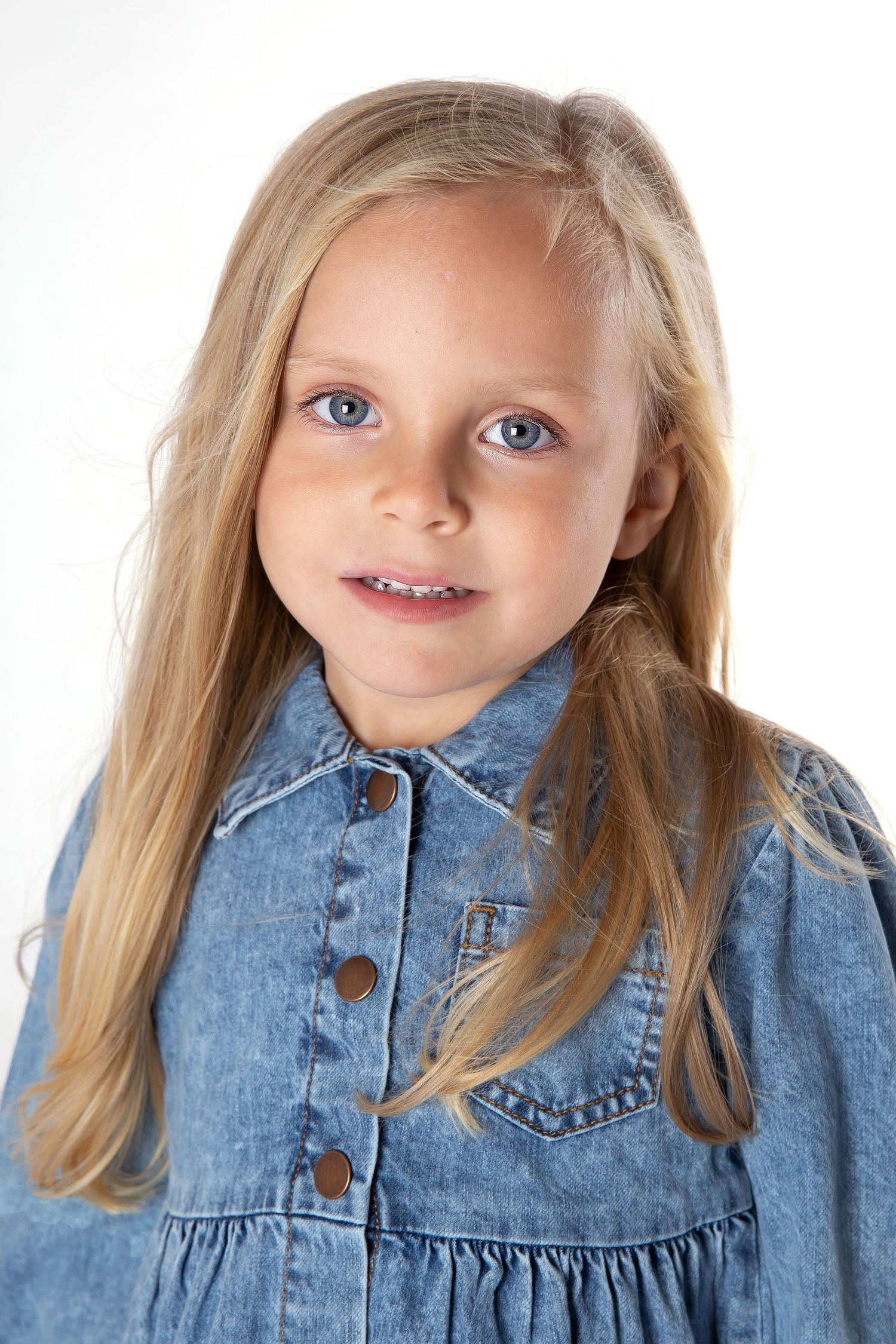 Young child with bright blue eyes wearing a casual denim button-up dress.
