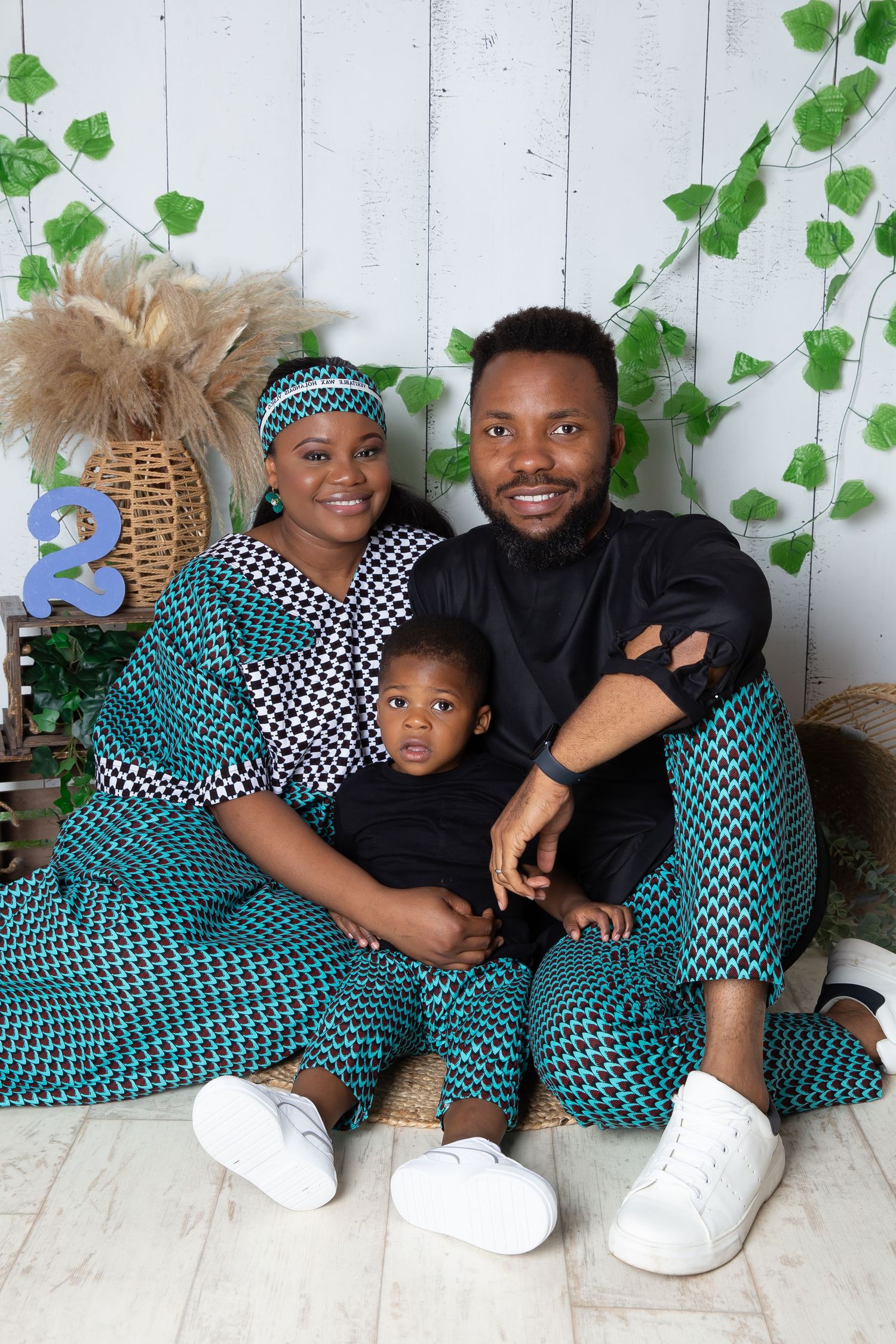 Four people wearing matching teal and checkered outfits sit together against a white wall with ivy decorations.
