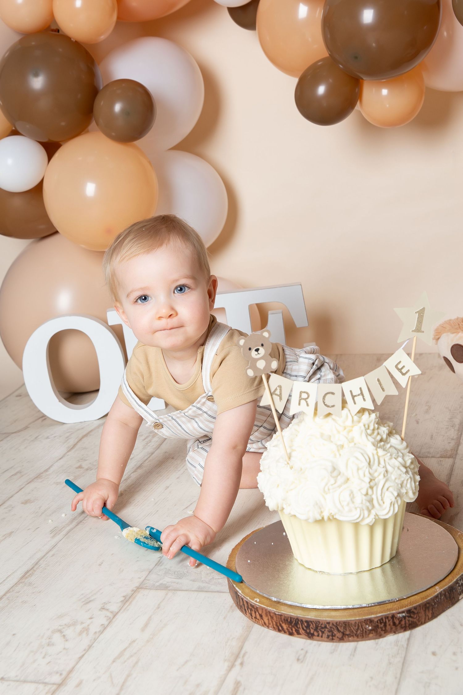 First birthday celebration setup with neutral balloons, giant cupcake and bunny decoration on wooden floor.