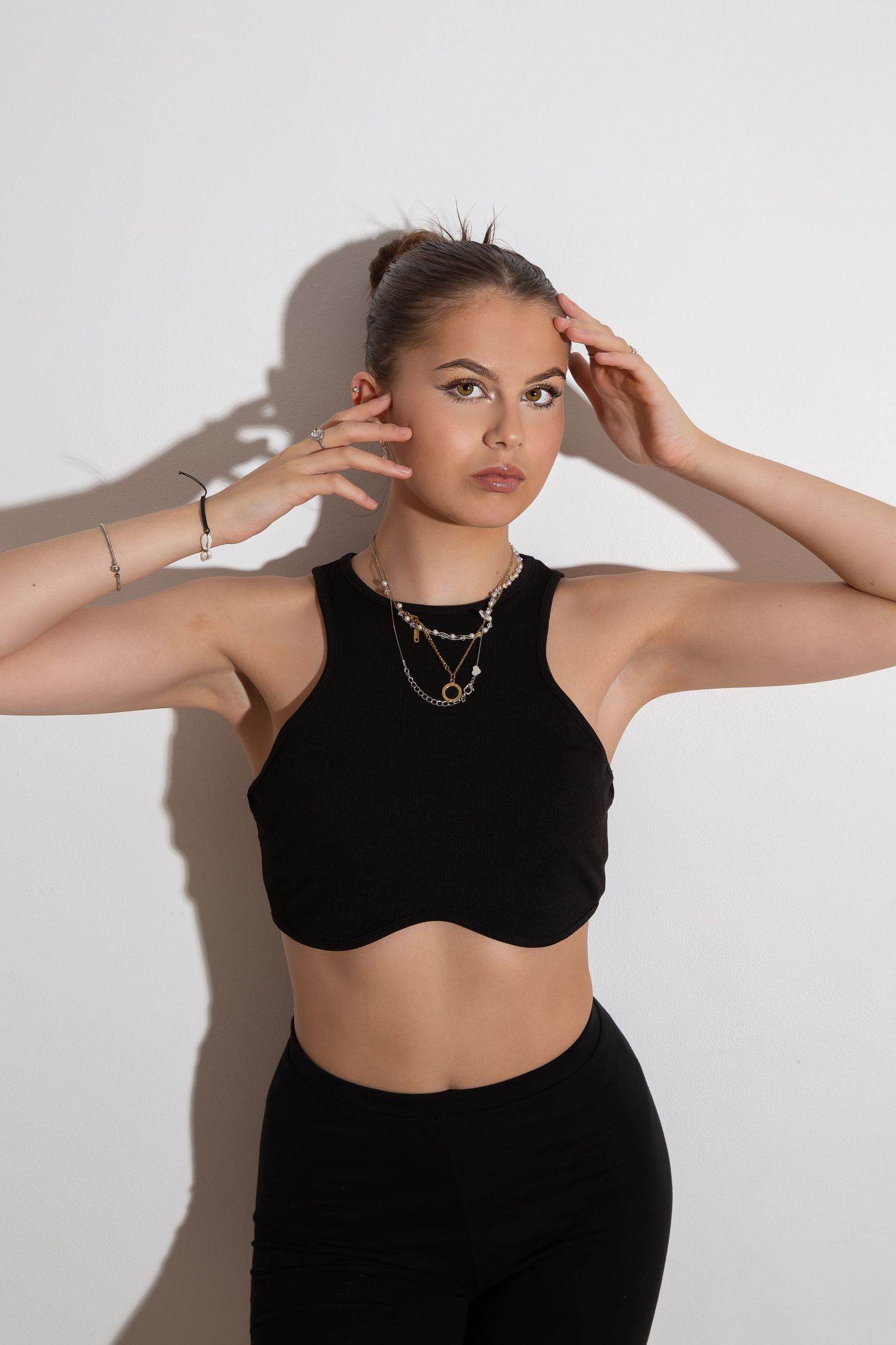 Studio portrait in black athletic crop top and pants with gold necklace against white background in moody lighting.