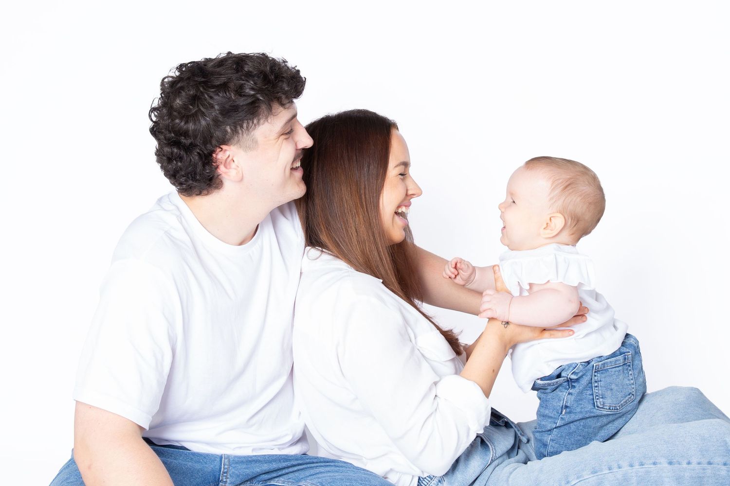 A loving family wearing white clothes lies together on a blue background while playing and sharing tender moments.