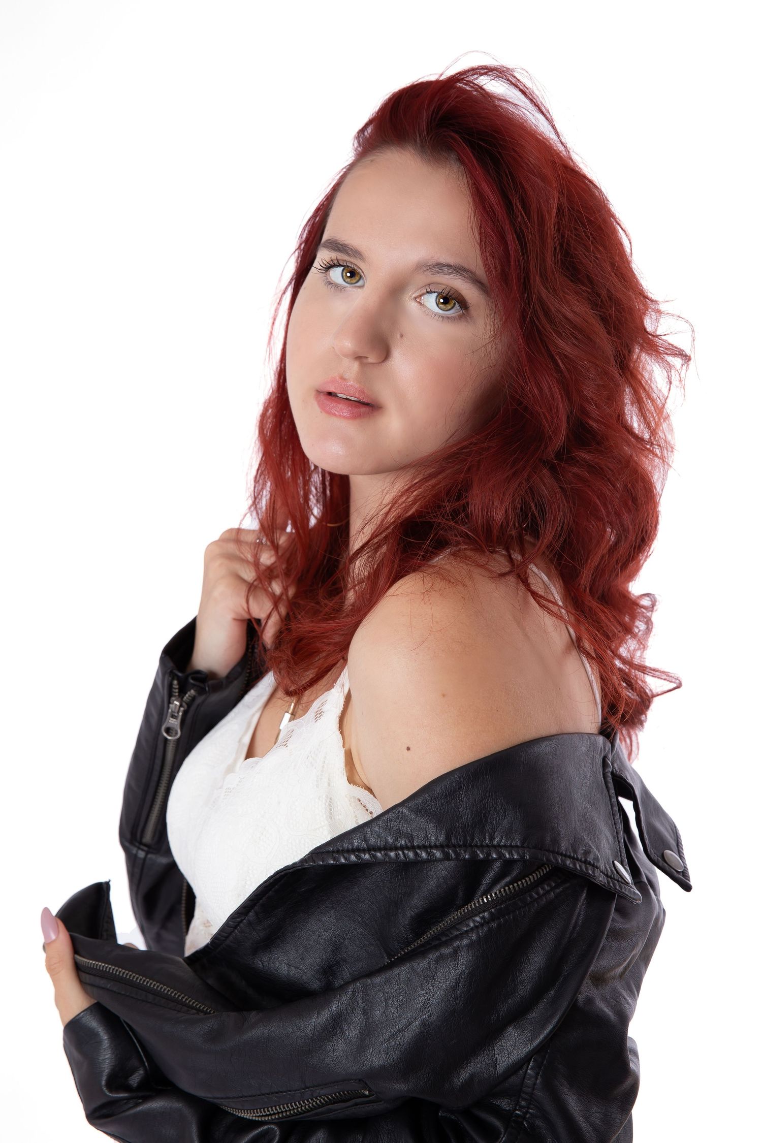 A fashion model with vibrant red hair poses in a black leather jacket against a white background.