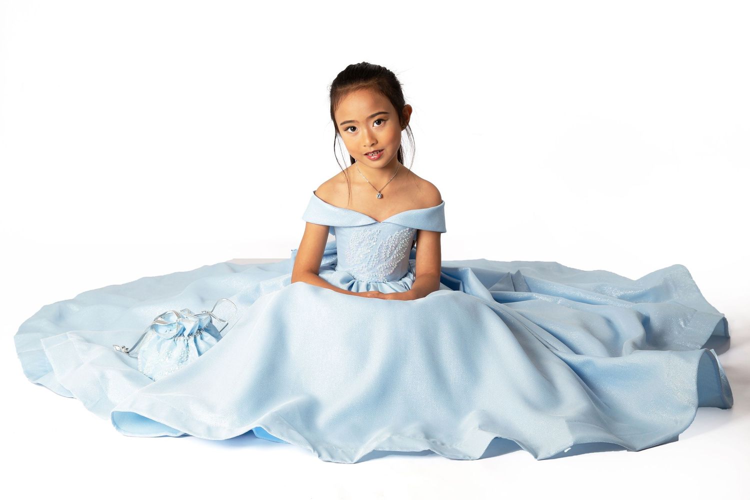 A young person wearing an elegant off-shoulder light blue ball gown sits gracefully on the floor.