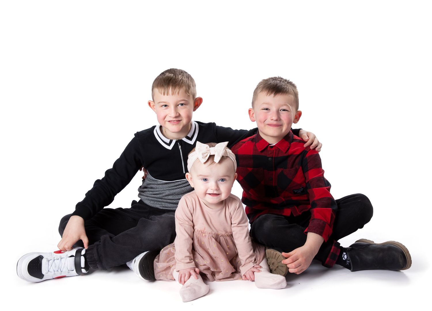 Three children in matching poses sitting together on a white background wearing casual clothing.