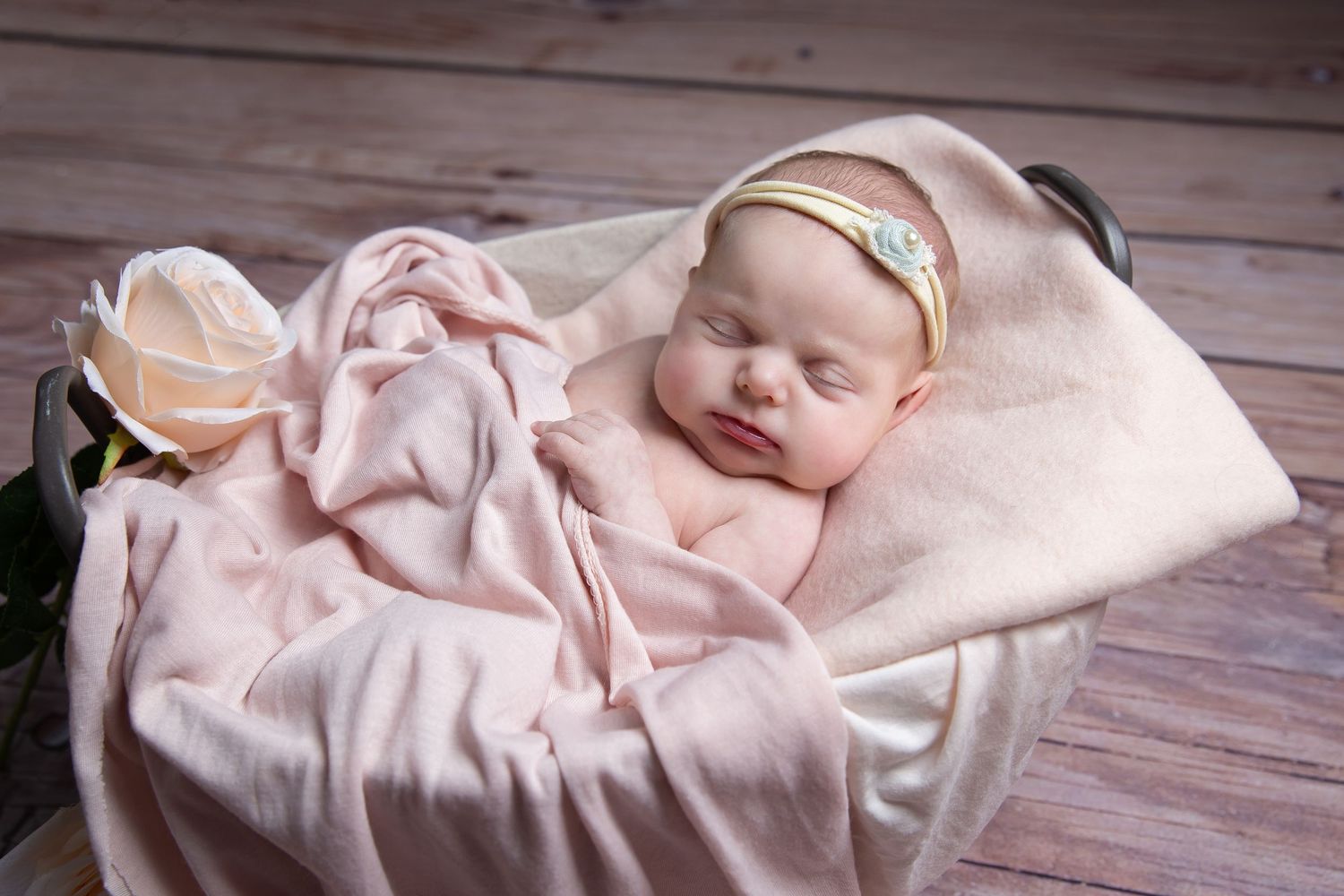 Seven artistic newborn photos showing a sleeping baby in soft pink blankets lying on wooden floor.