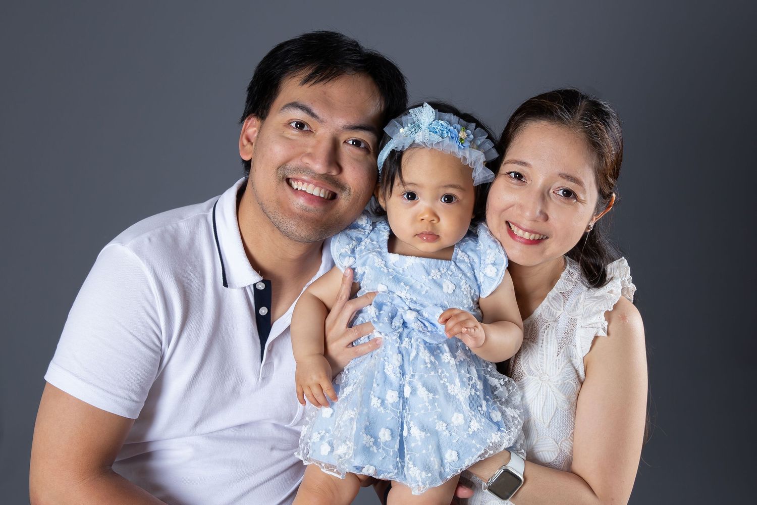 Happy Asian family posing together in studio against gray background.