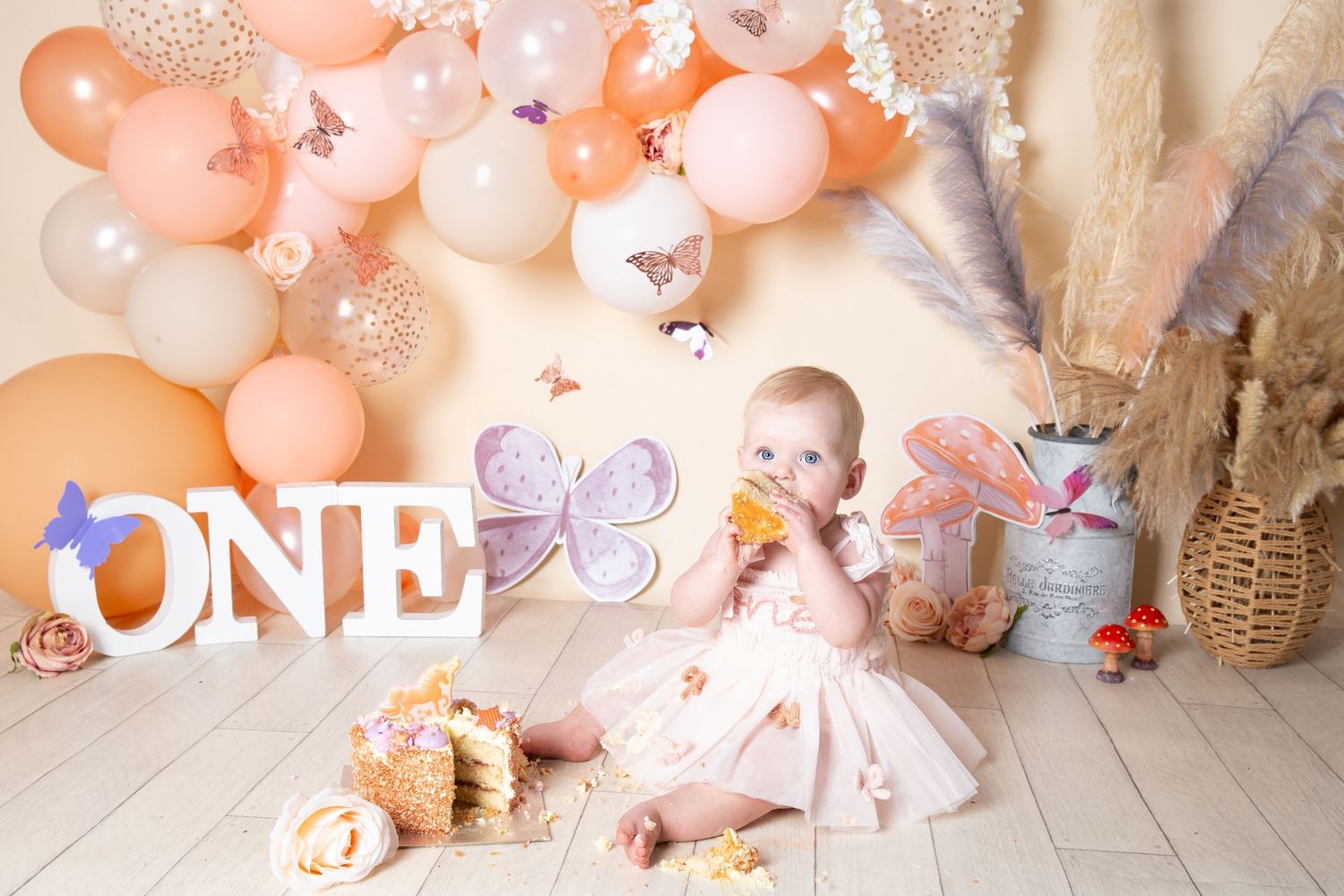 Pink and rose gold balloon decorations with stuffed animals create a festive first birthday party setup.