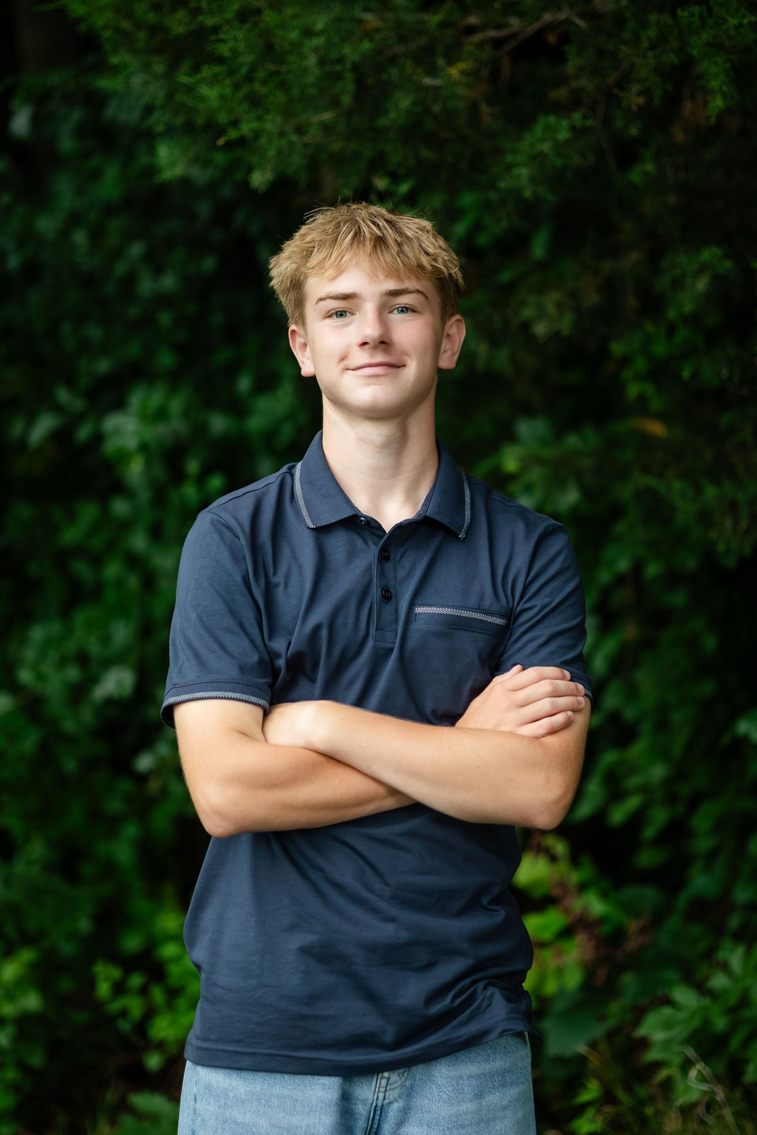 Person in navy polo shirt smiles confidently against green natural background.