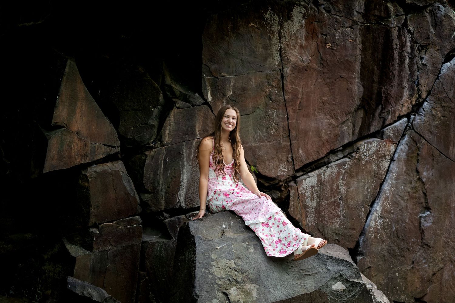 Person in pink dress sits gracefully against dramatic rock formation.