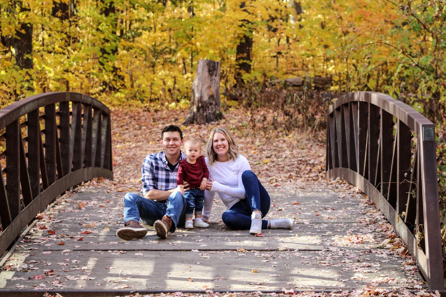 Family photo session on wooden bridge surrounded by autumn foliage.