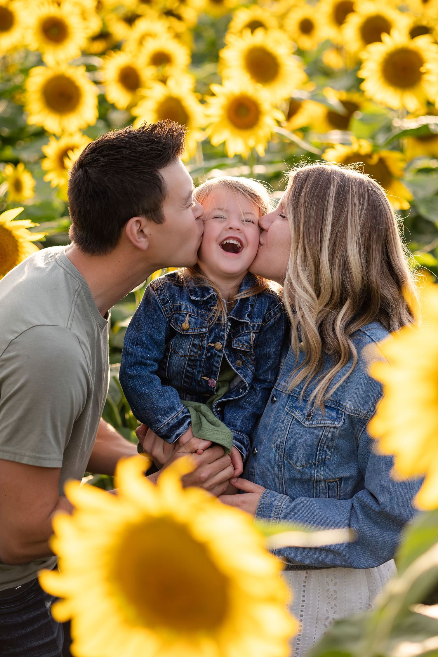 Joyful family sharing kisses and laughter among bright yellow sunflowers.