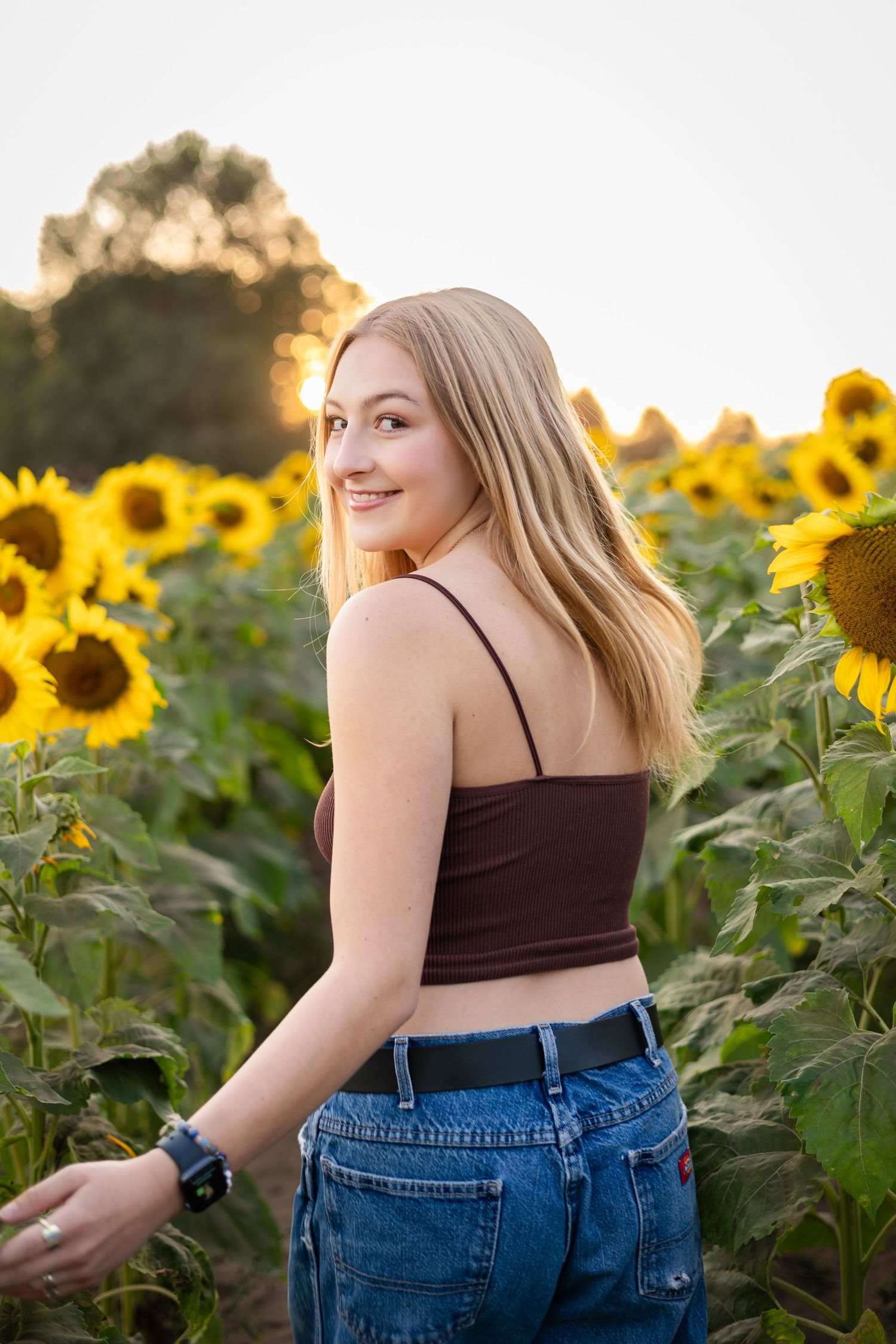 Candid portrait among blooming sunflowers during golden hour.