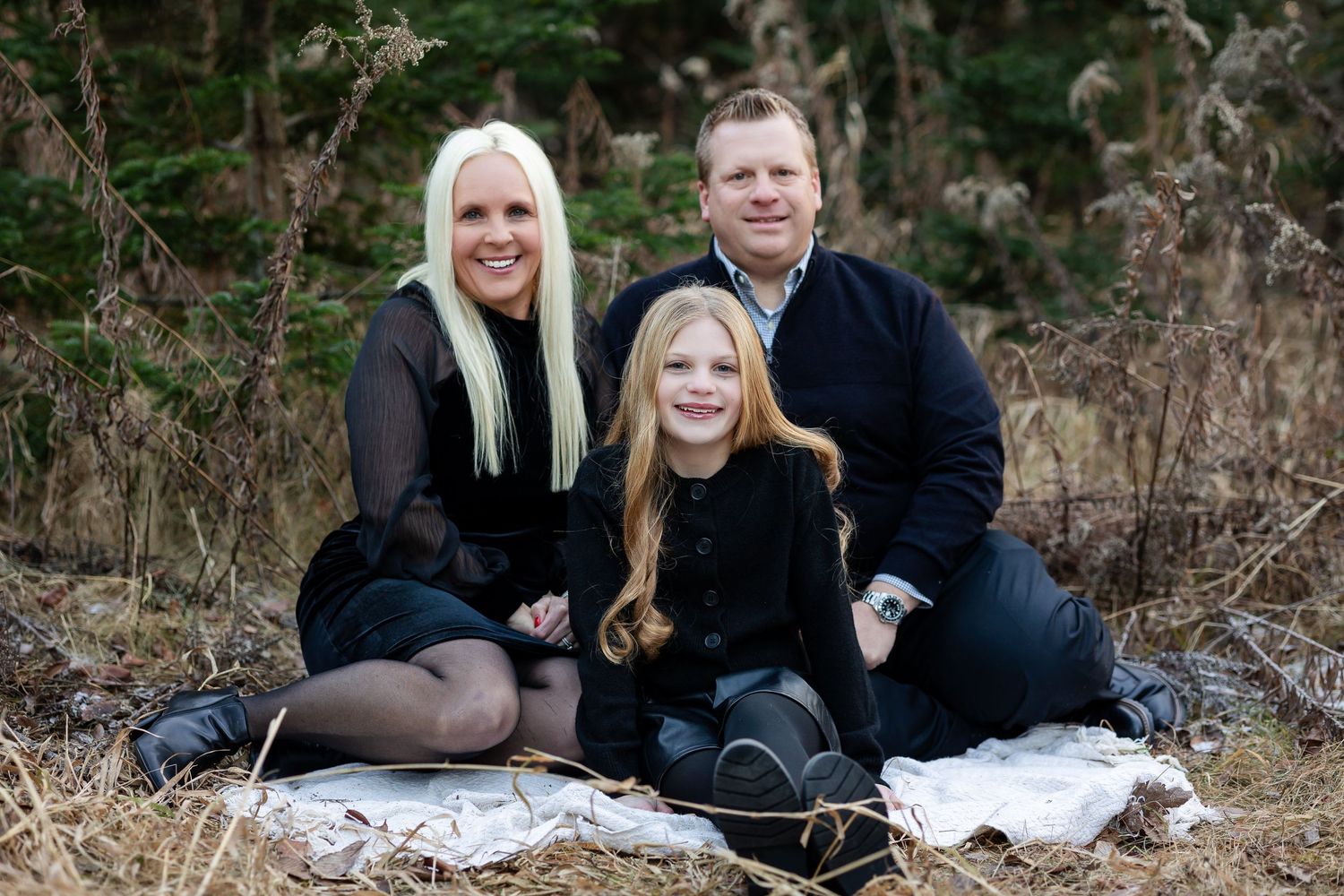 Family group poses together on a white blanket outdoors during a winter photo session.