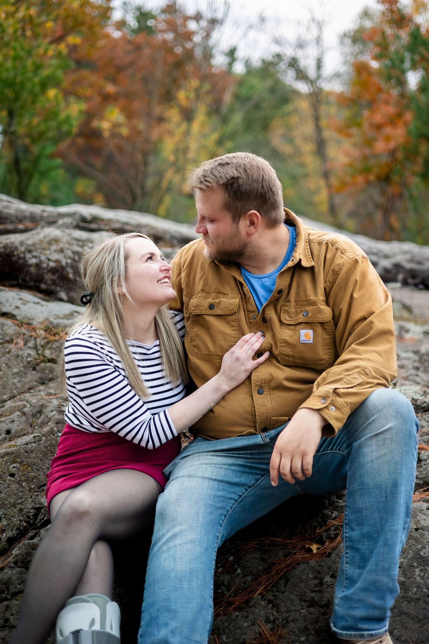 Couple sitting on rocks in autumn forest, gazing at each other affectionately.