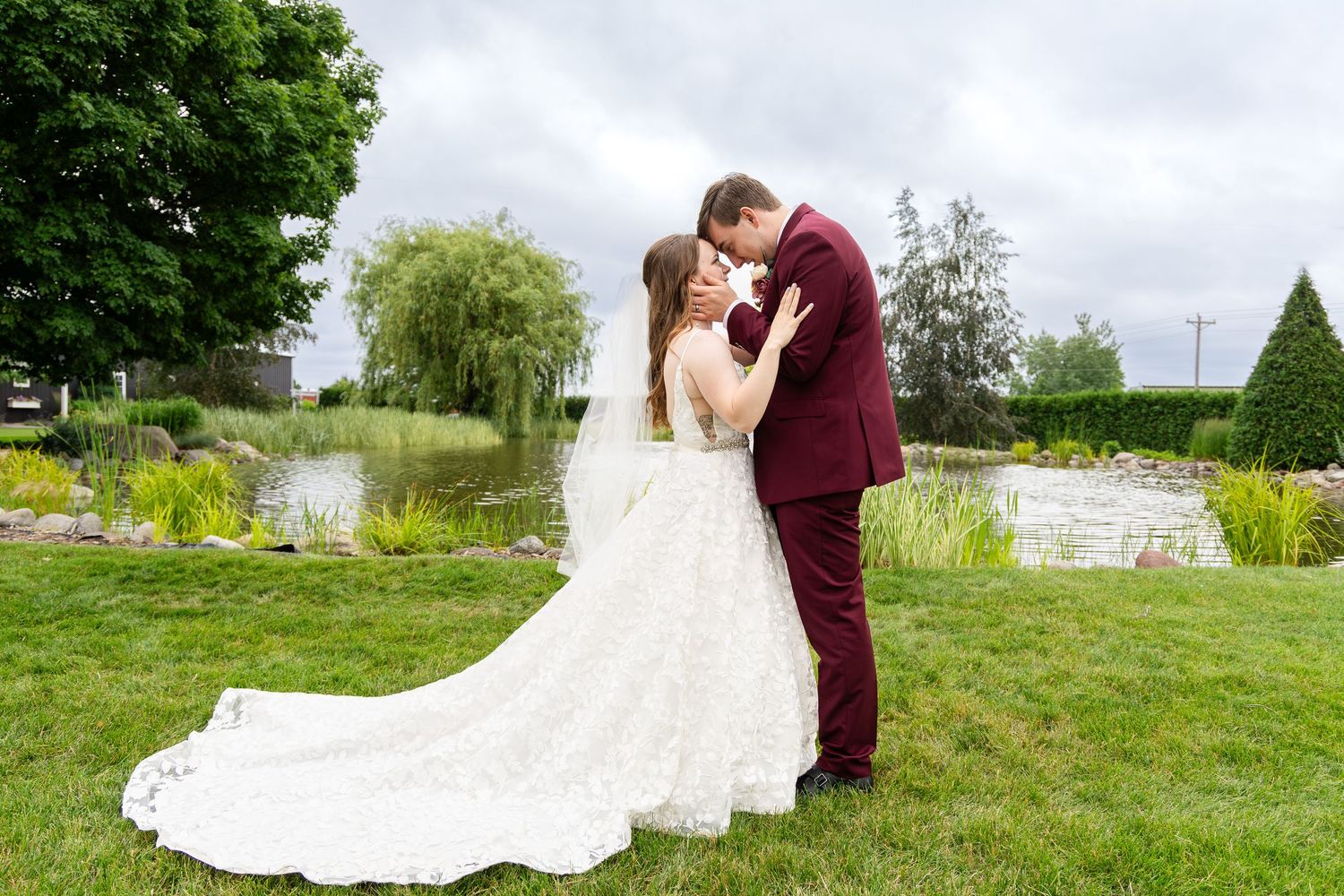 A couple shares an intimate moment in a lush garden setting wearing burgundy and white wedding attire.