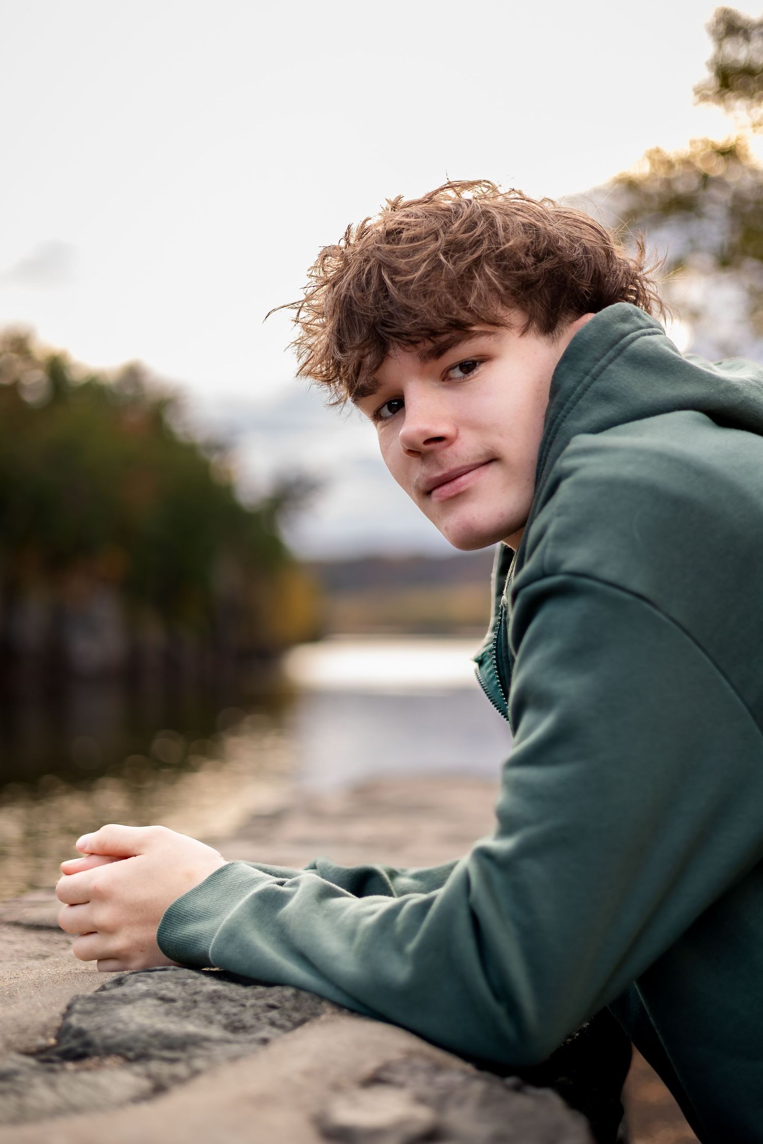A person in a green hoodie lies on their side near the water's edge during golden hour.