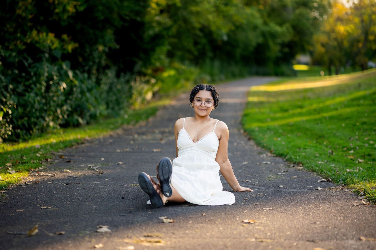 A child in a white dress plays in a park during autumn while golden sunlight filters through the trees.