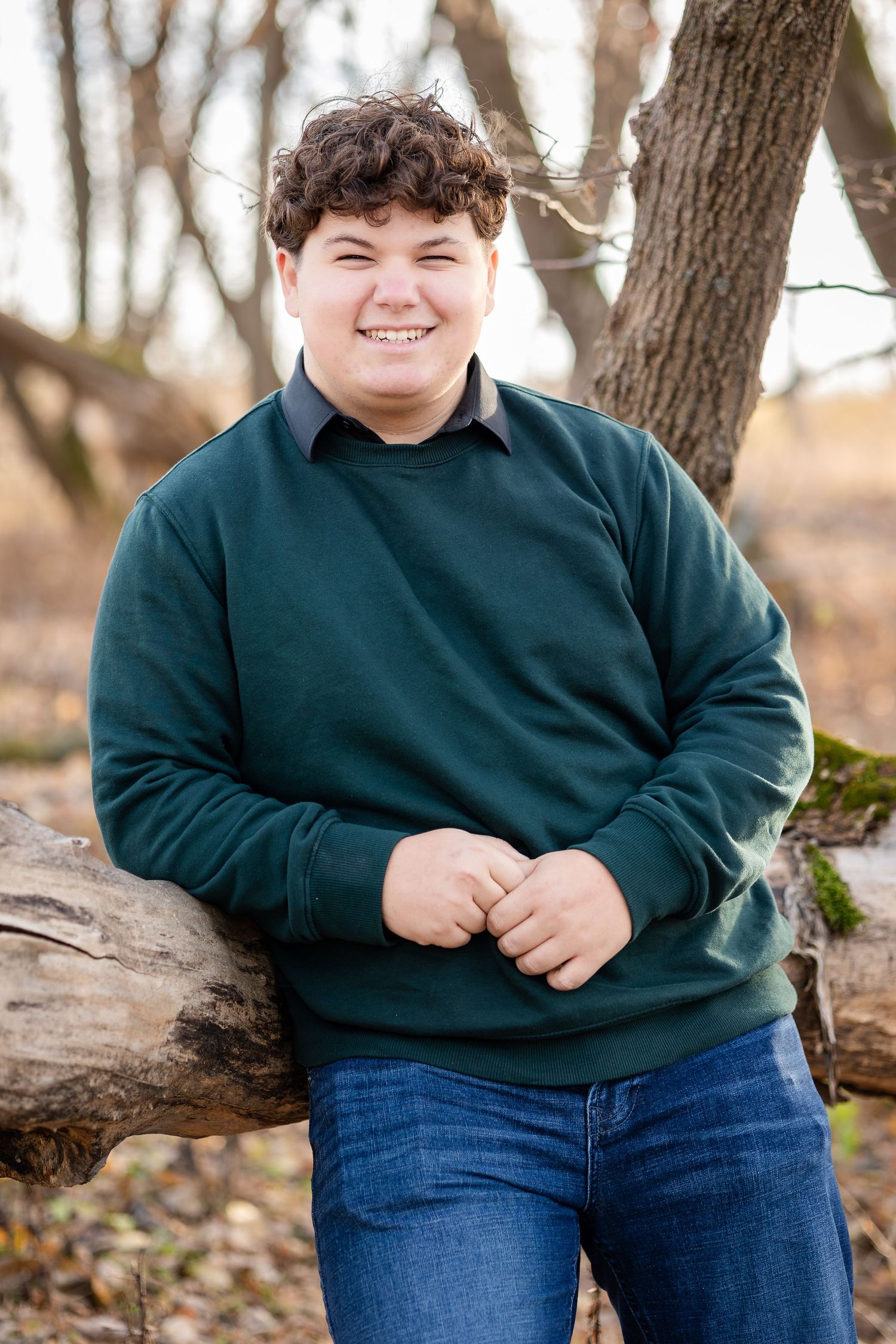 Person in dark green sweater sitting on fallen log in autumn forest setting.