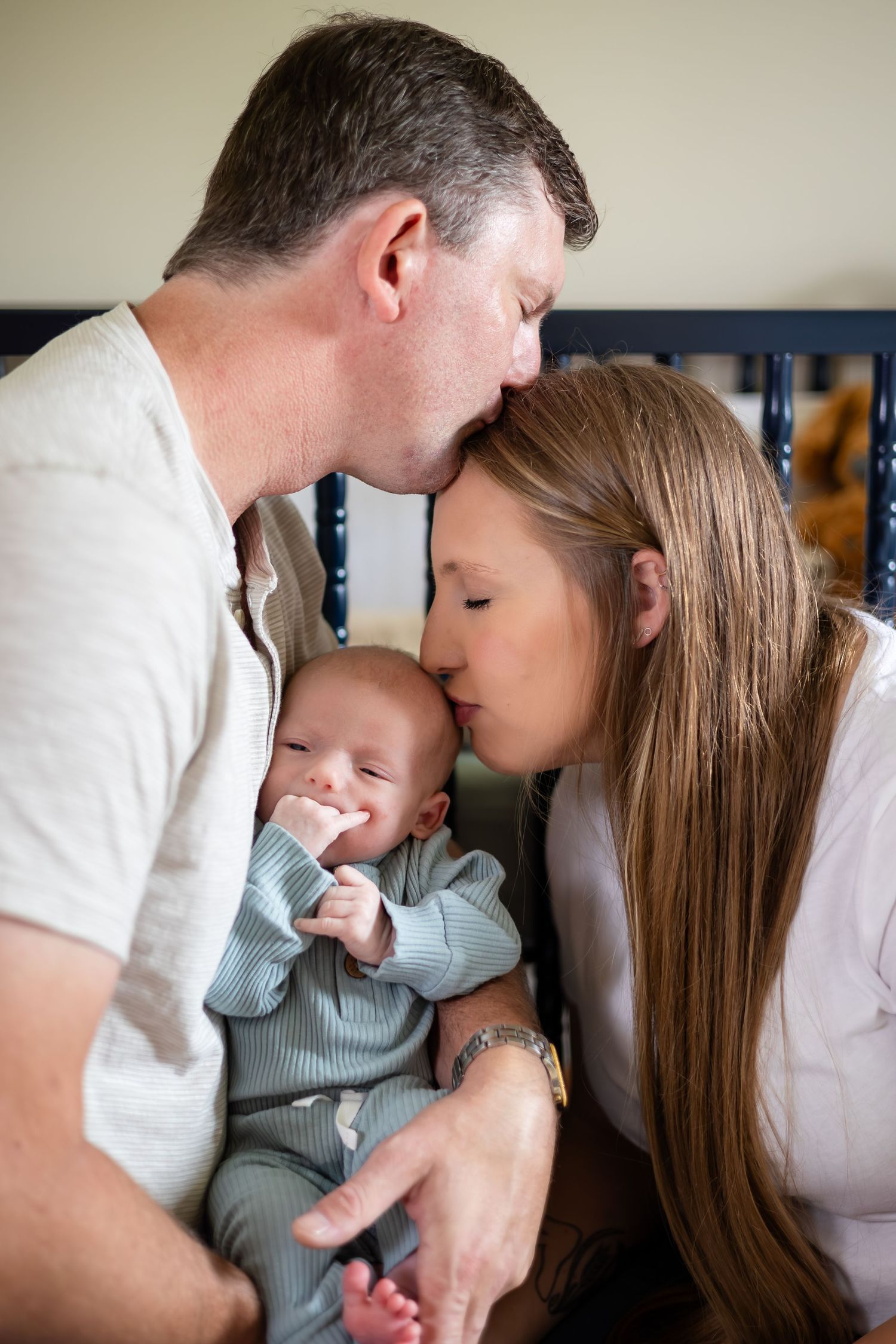 Intimate family moment with parents cuddling their baby in soft natural light.