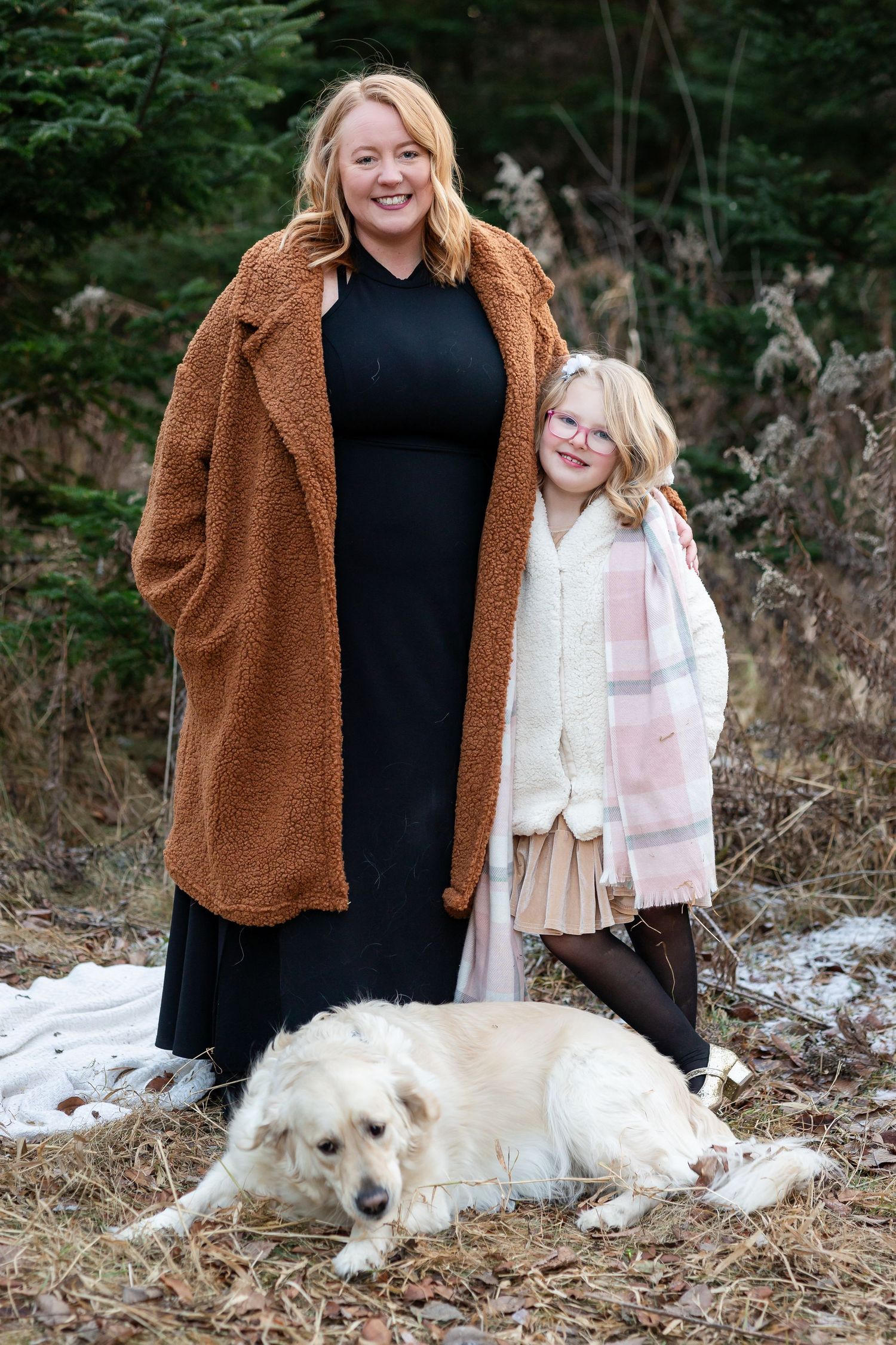 People in winter coats pose with a white dog lying in the fallen leaves.