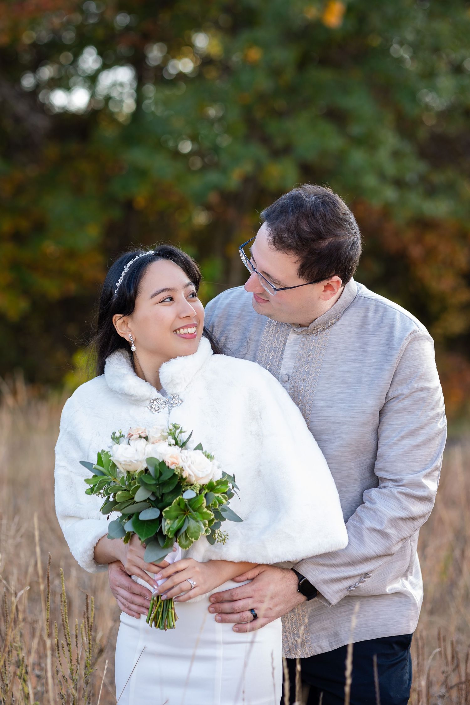 A couple poses with a white bouquet in a field of tall autumn grass.
