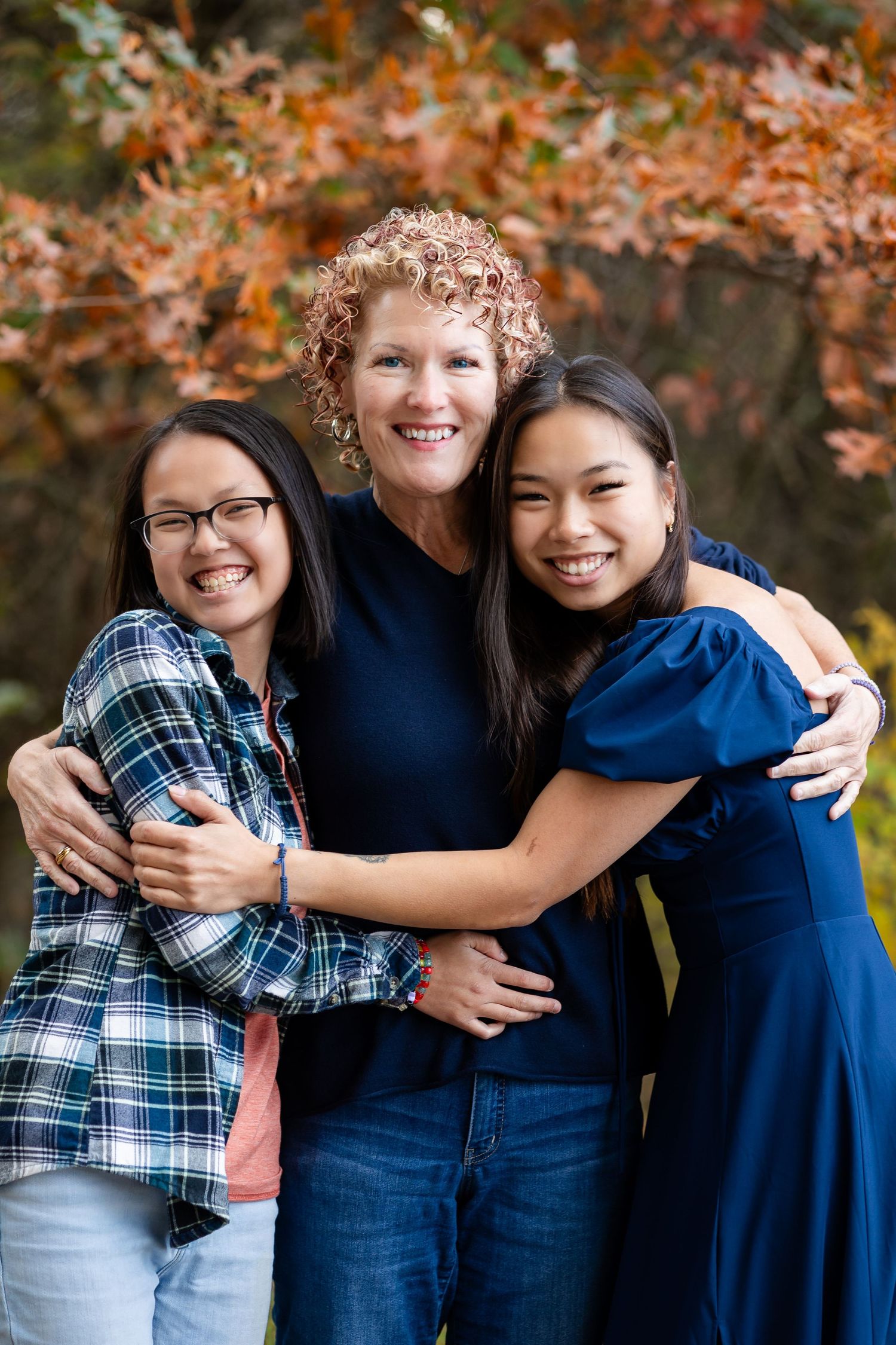 Friends embracing and laughing together in front of fall colored trees.