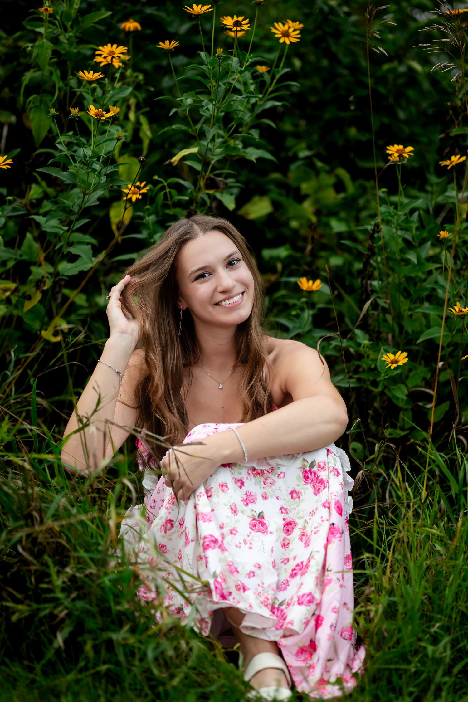 Person in white and pink dress poses elegantly among yellow wildflowers.