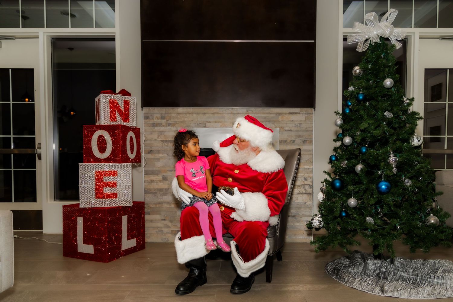 Holiday photo session setup with Christmas decorations including a tree, NOEL letters, and Santa's chair.