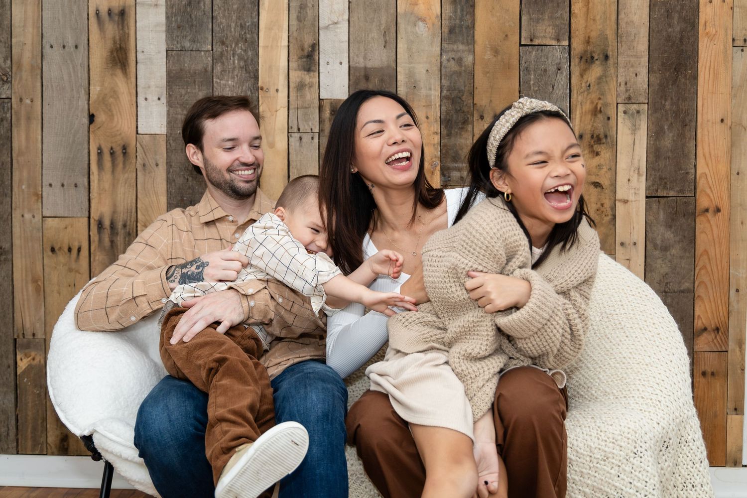 A group of friends laugh together while sitting on a wooden bench during a casual gathering.