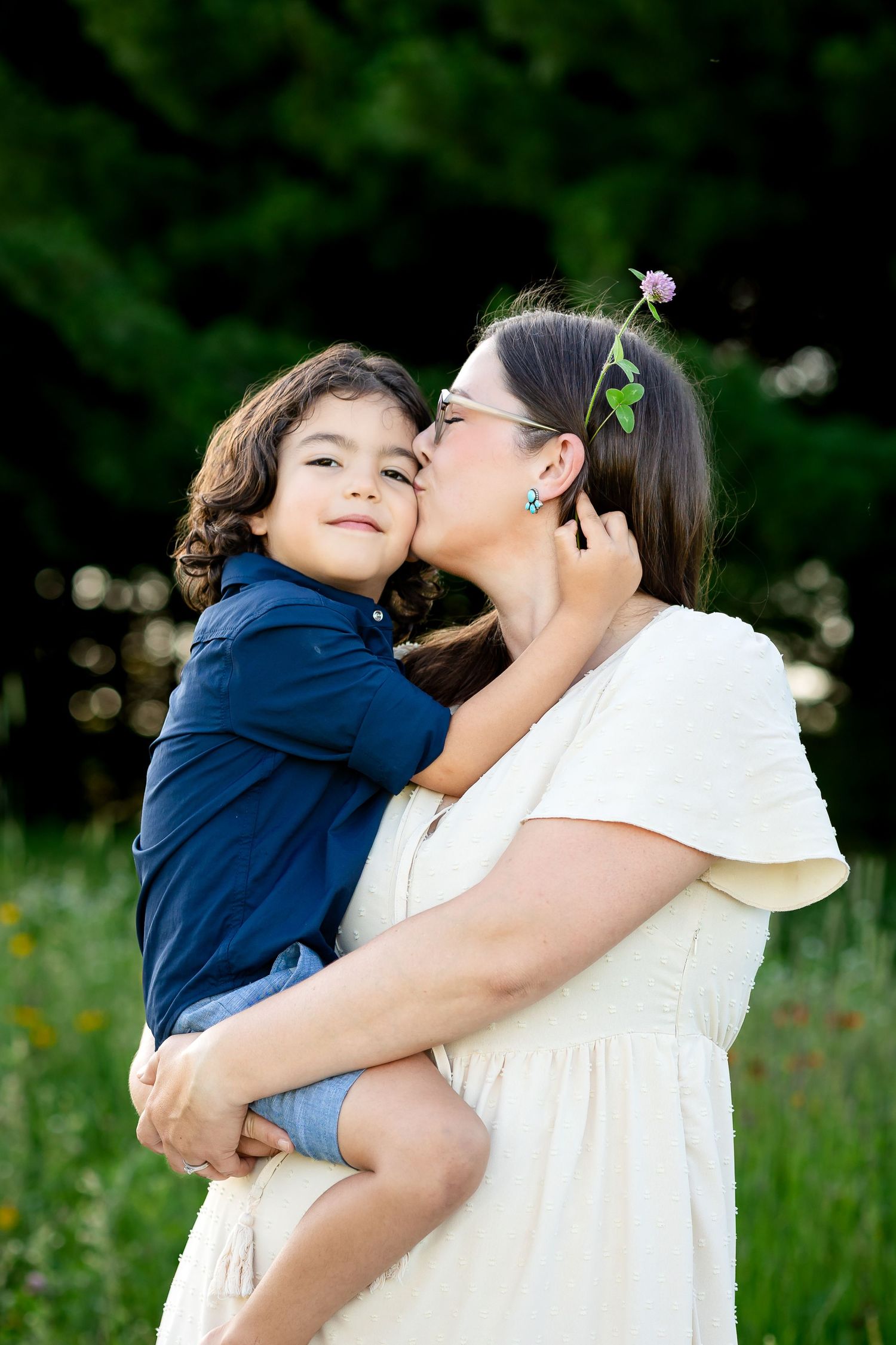 A tender moment of affection and laughter shared between a parent and child in a lush green outdoor setting.