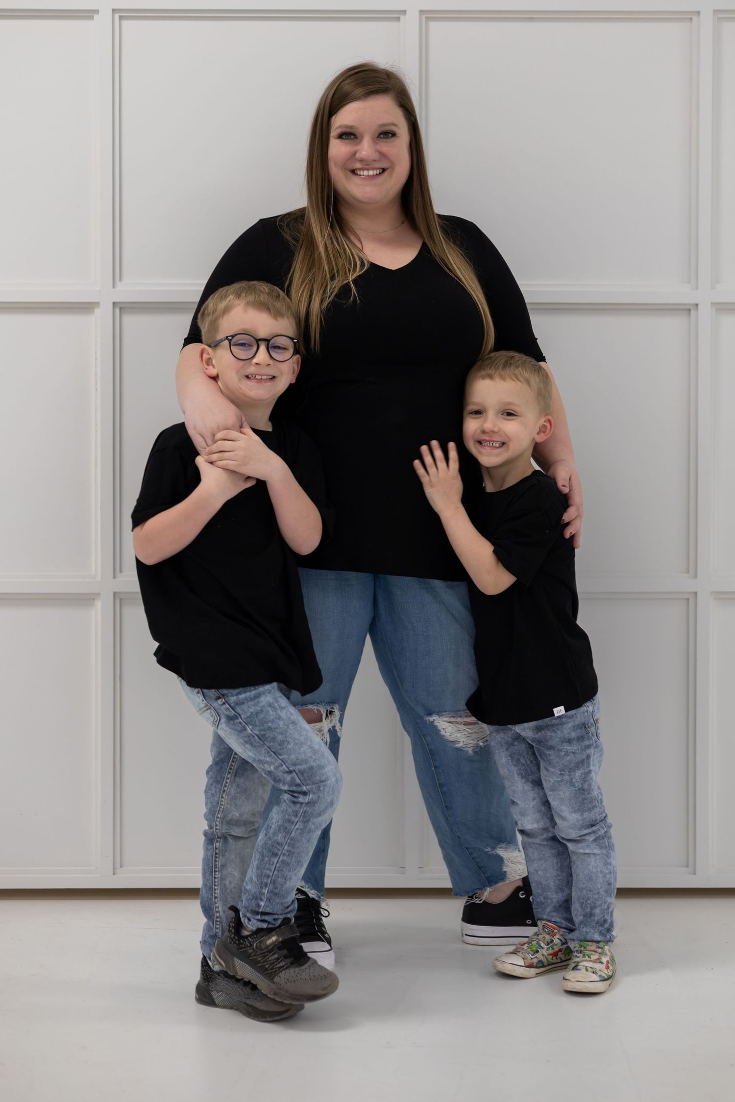 Family members in black tops and jeans posing against a white paneled wall.