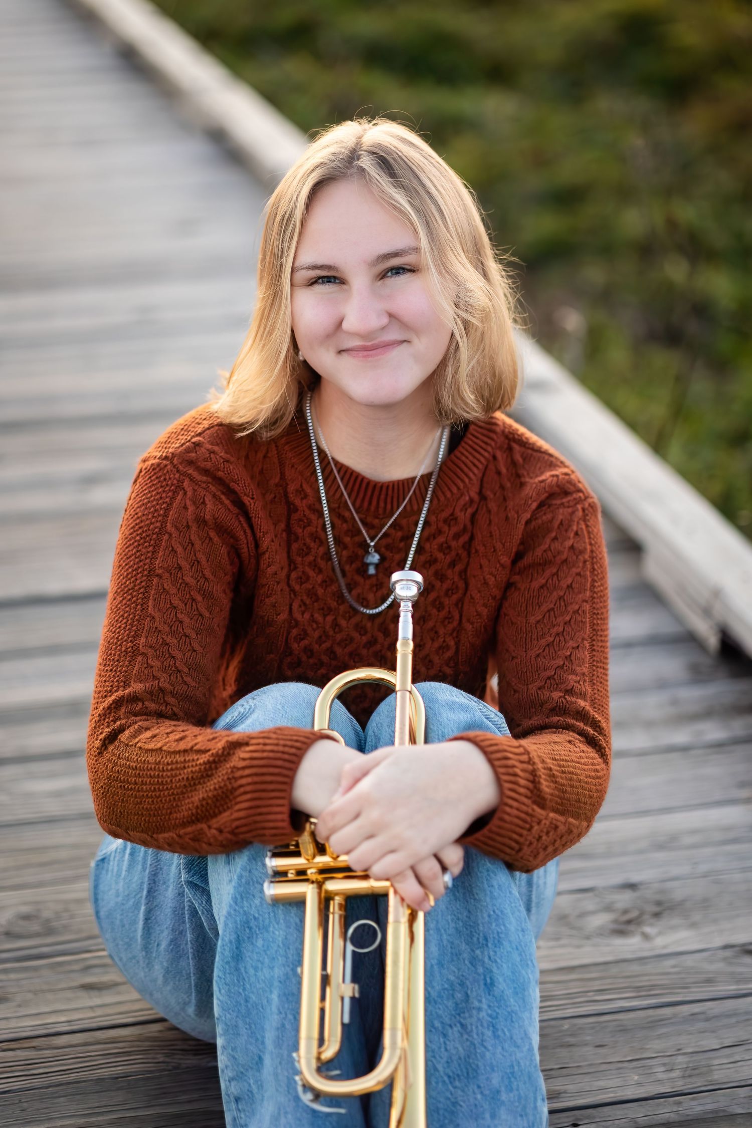 A casual portrait series on a wooden deck featuring someone in a brown sweater holding a brass trumpet.
