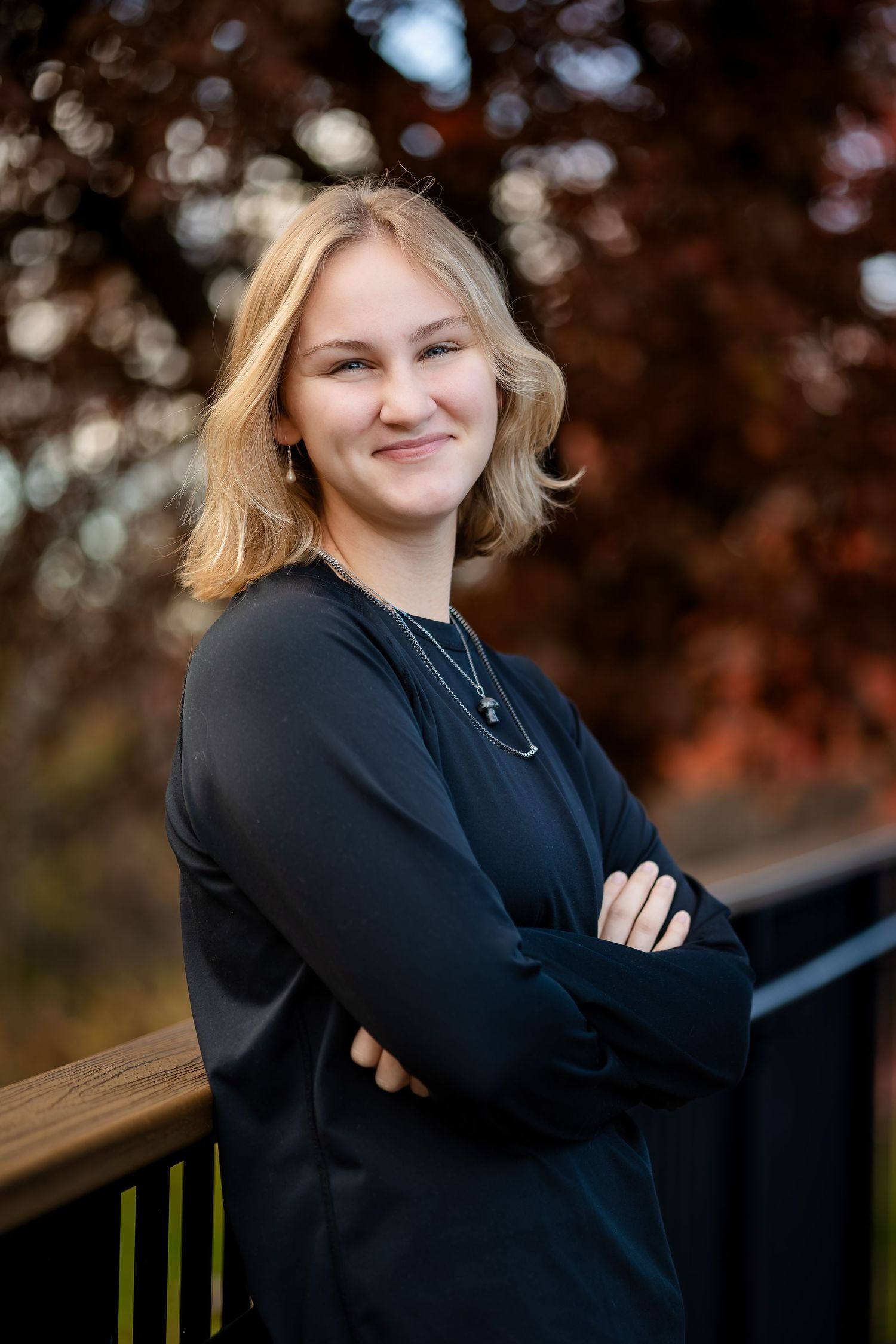 A person in a black sweater poses outdoors against an autumn backdrop with blurred bokeh lighting effects.