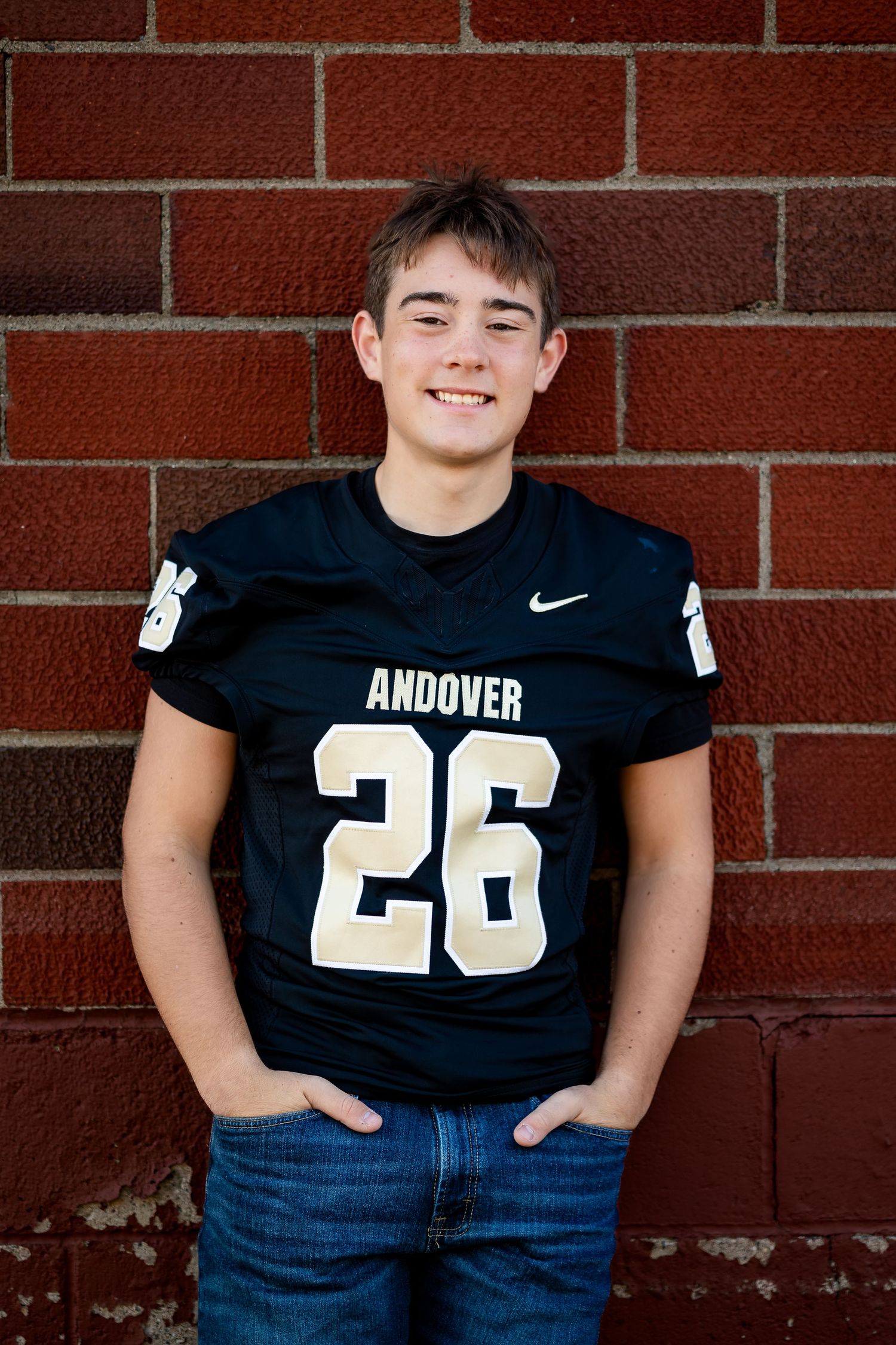 Cropped view of person wearing Andover football jersey number 26 against red brick wall.