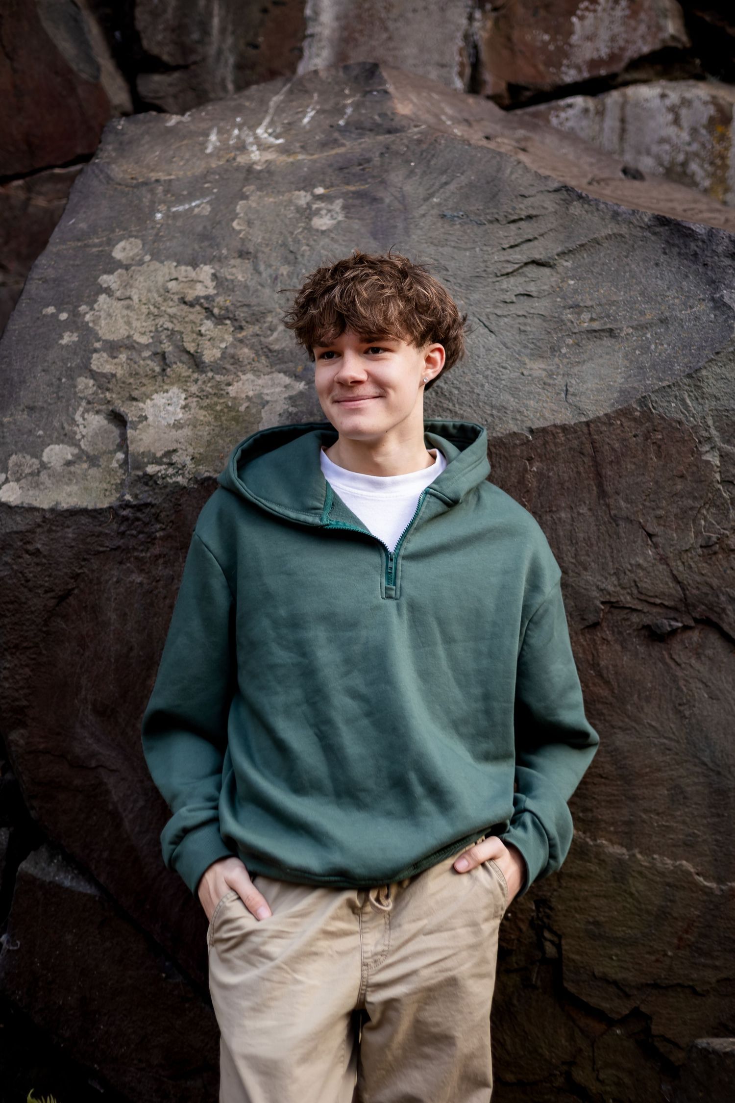 A series of casual portrait shots against a dark stone wall showing someone in a green hoodie and khaki pants.