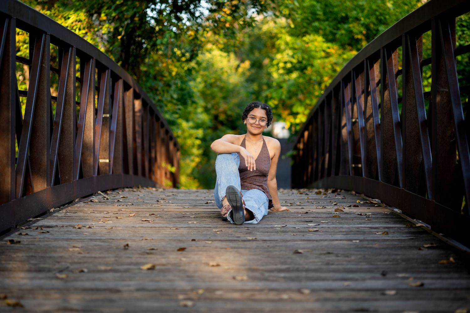 A person in athletic wear stretches on a wooden footbridge surrounded by lush green trees and foliage.