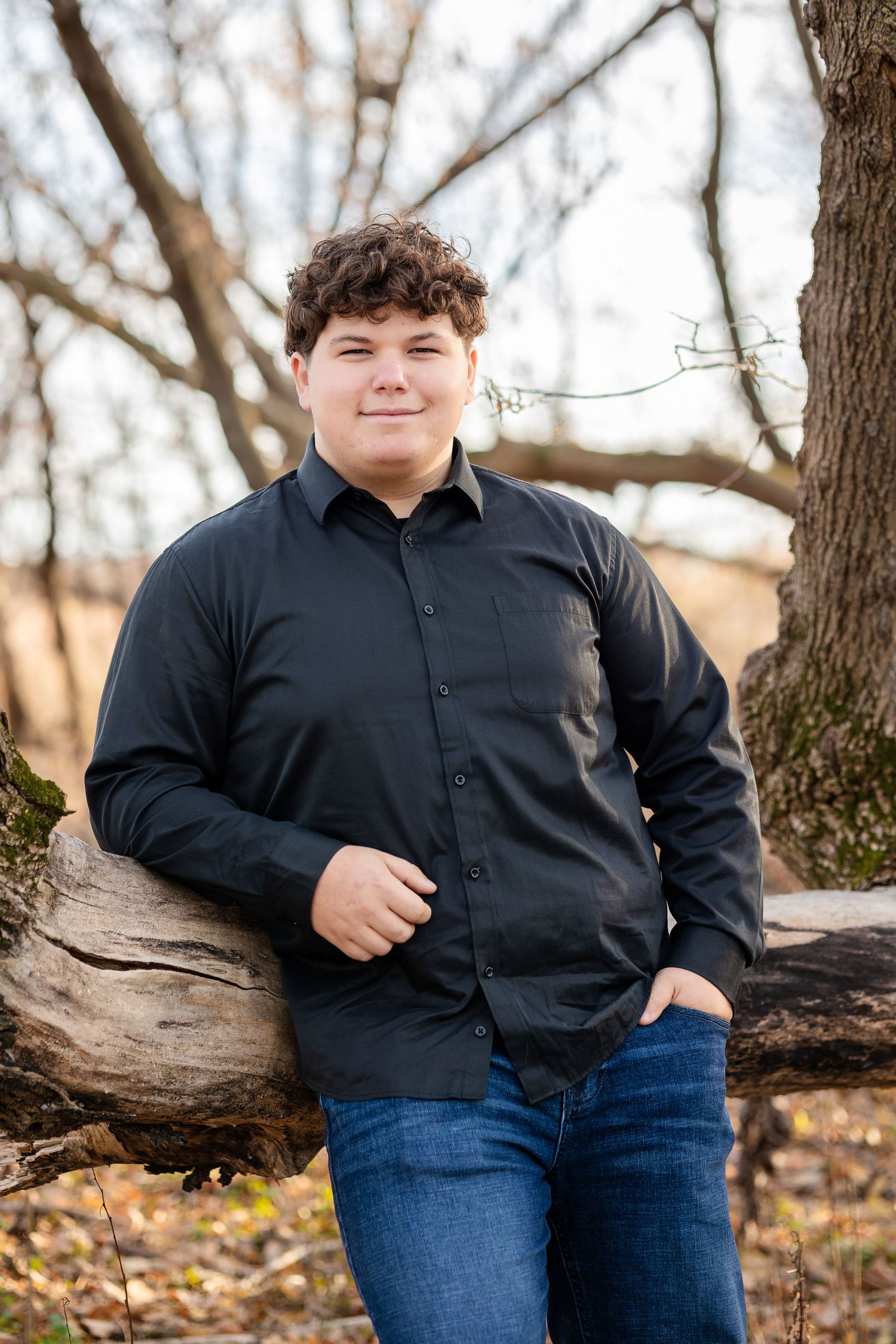 Person in black button-down shirt and jeans standing against natural woodland backdrop.