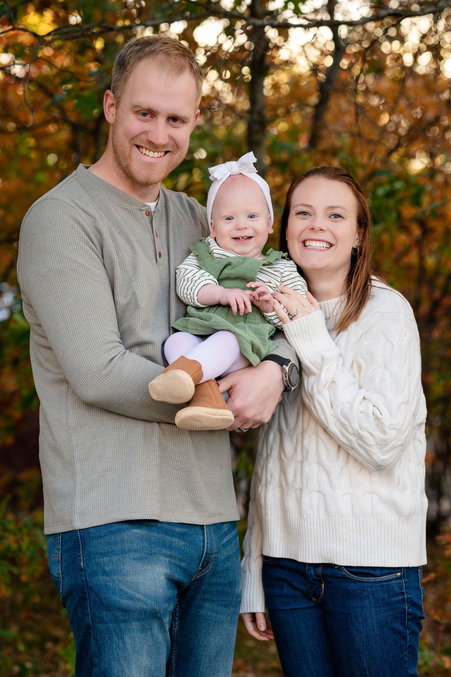 A family portrait in autumn featuring parents holding a baby wearing a green outfit.