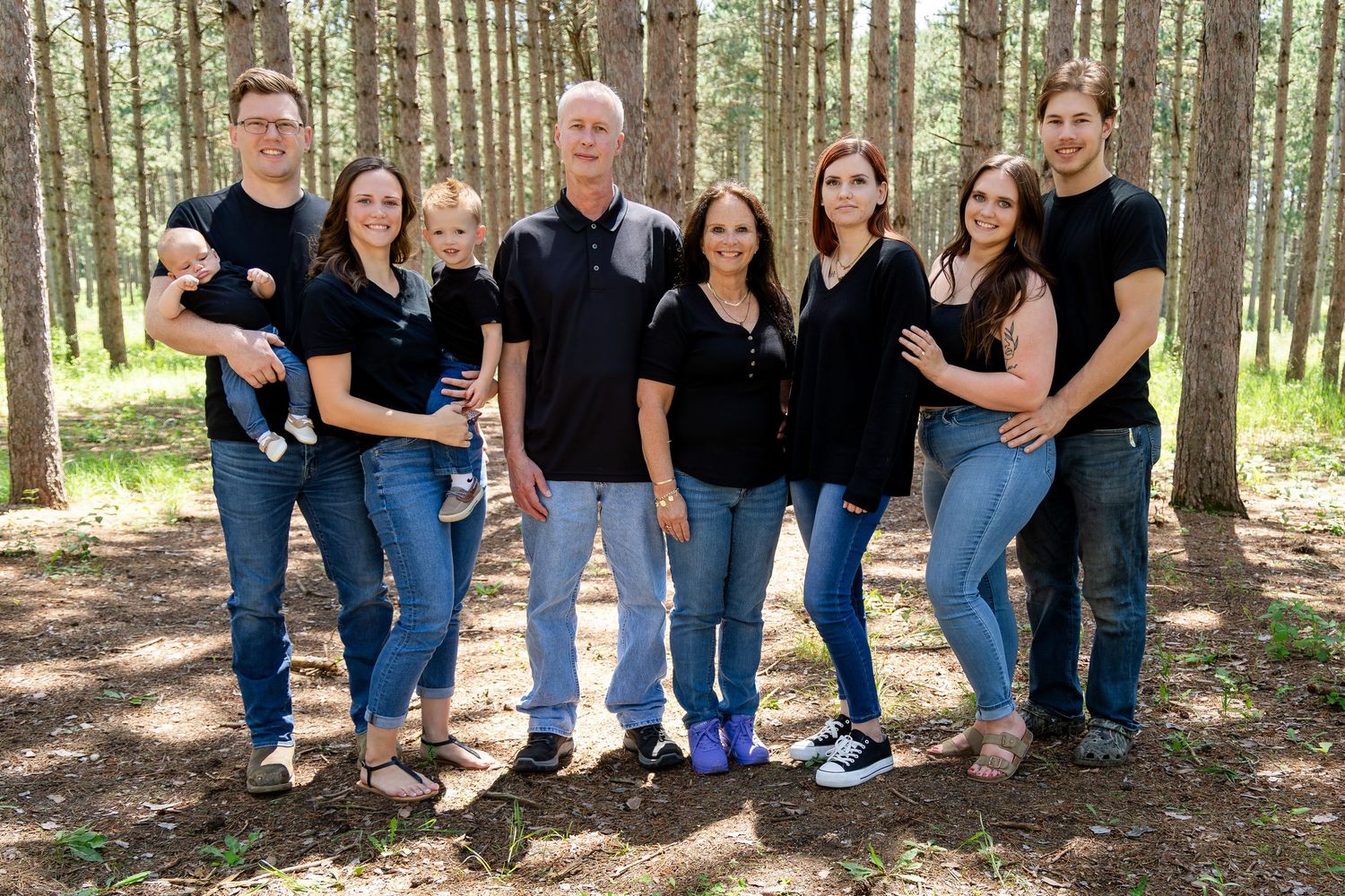 Group photo of family members wearing matching black shirts in pine forest.