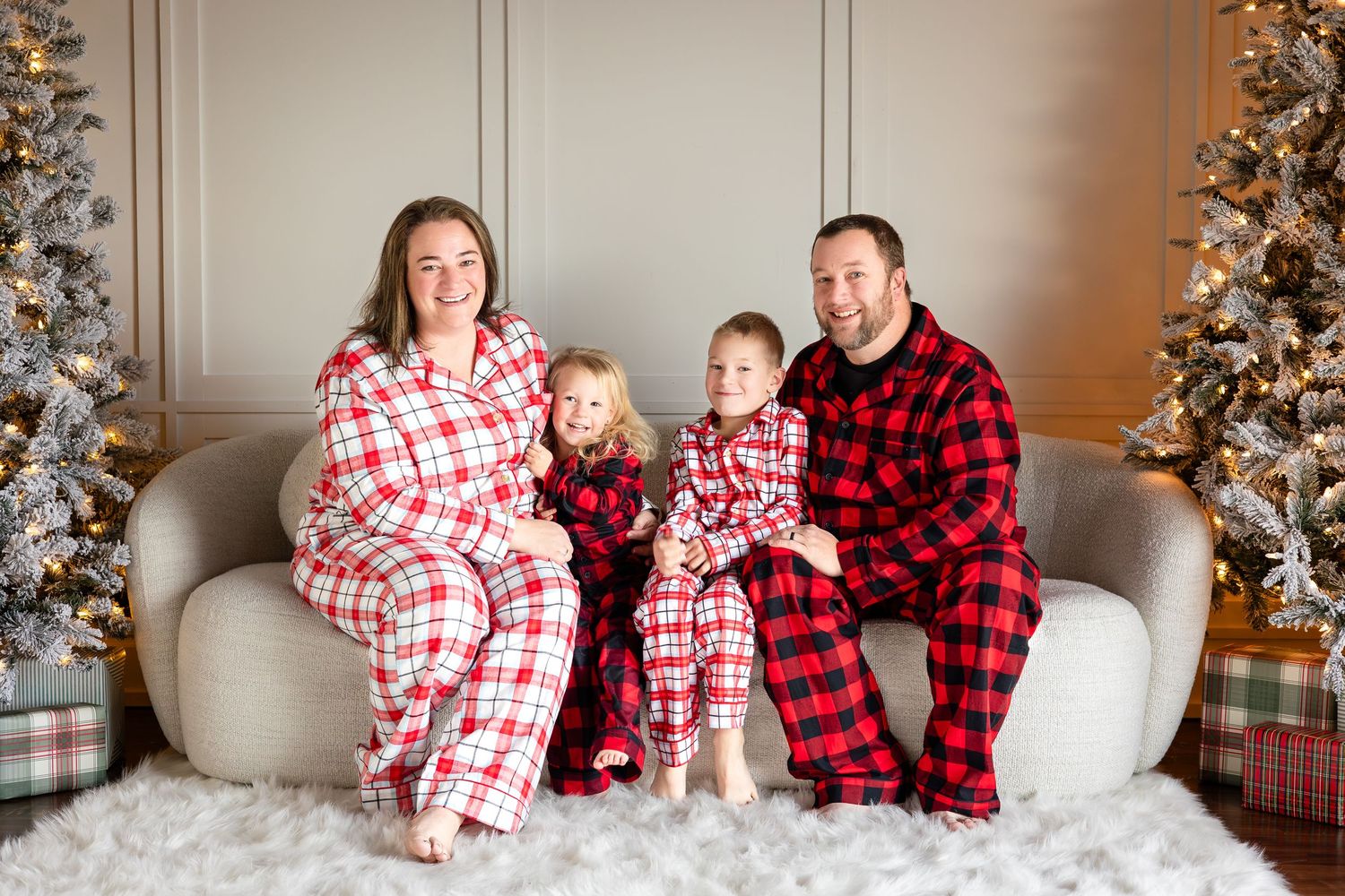 Family wearing matching red and white plaid Christmas pajamas pose by decorated tree.