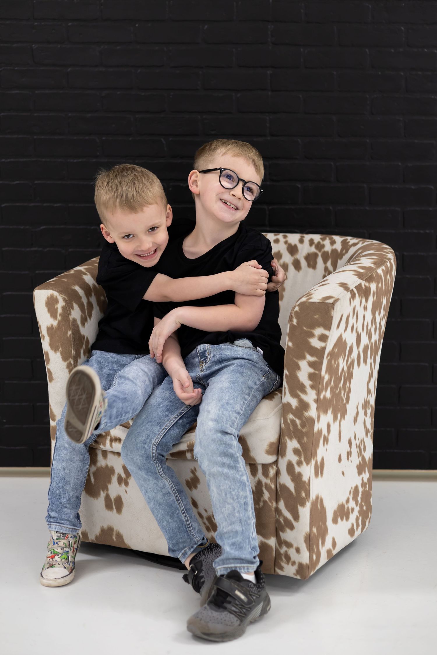 Children sitting on a brown and white cowhide armchair against a black wall.