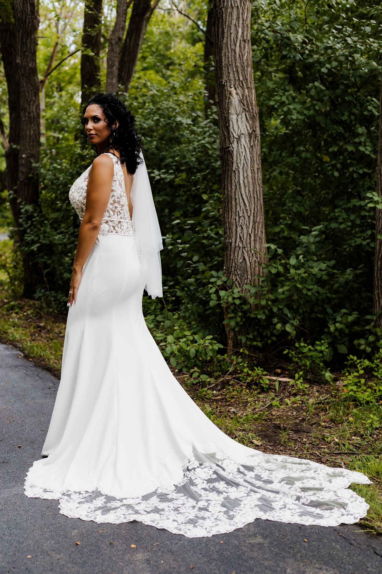 Beautiful wedding dress with lace details and long train photographed in a forest setting.