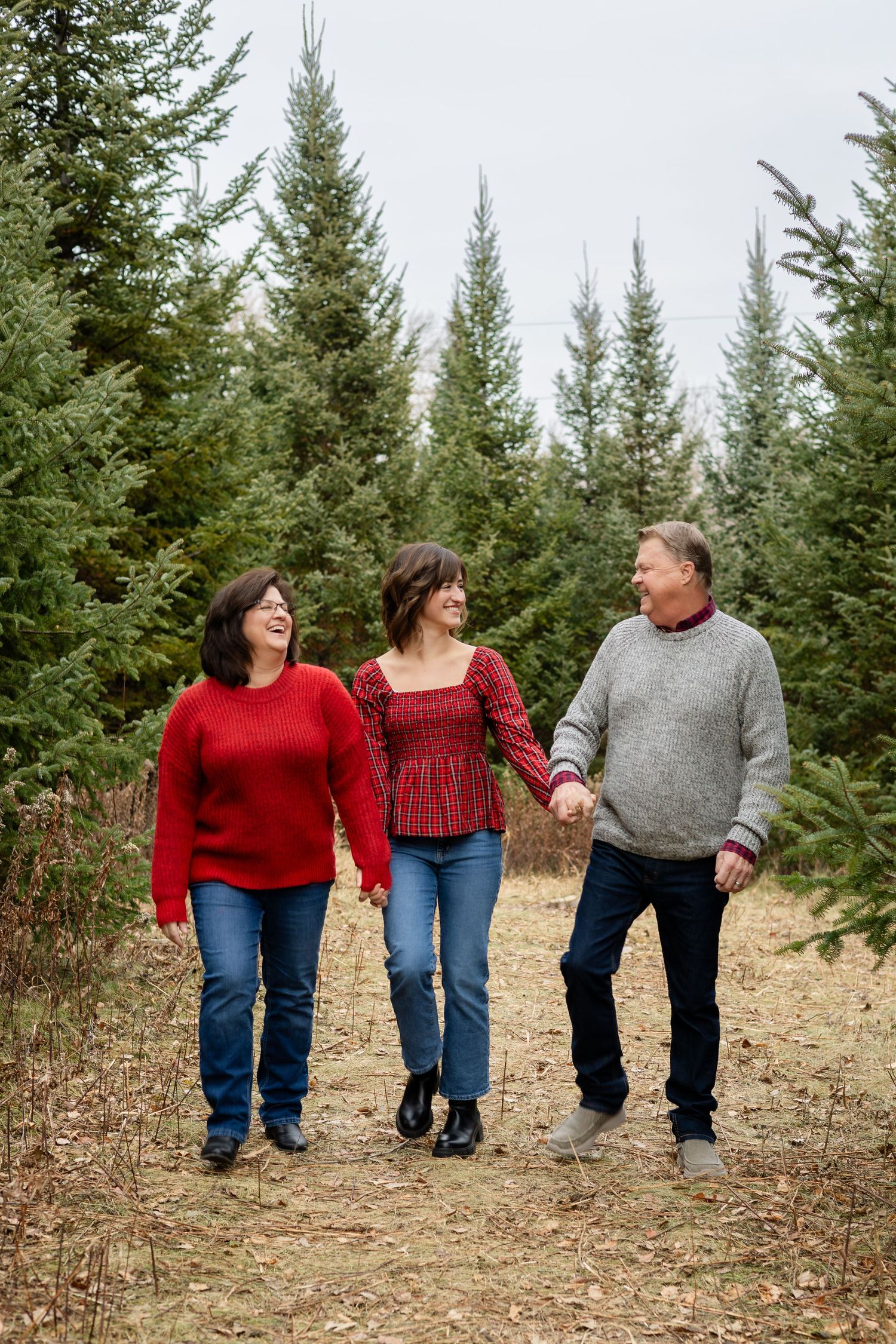 Three people in casual winter attire walking together along a path with evergreen trees in background.
